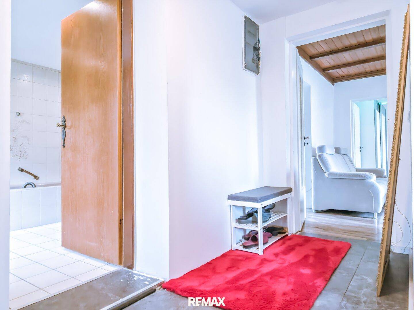 Flur mit Zugang zu einem Badezimmer, ausgestattet mit Schuhbank und Spiegel.