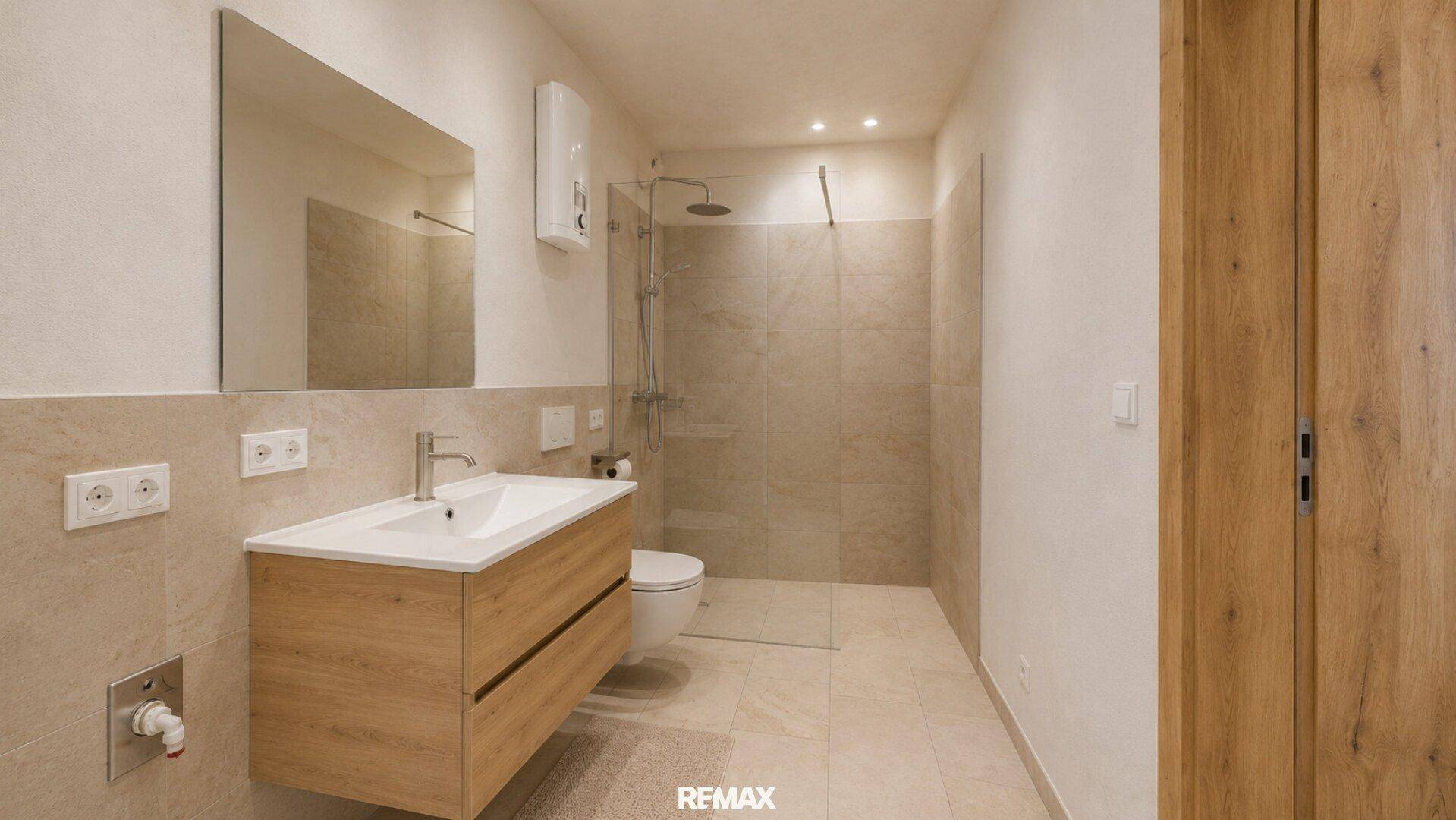 Modernes Badezimmer mit begehbarer Dusche, schwebendem Waschtisch und großen Fliesen.