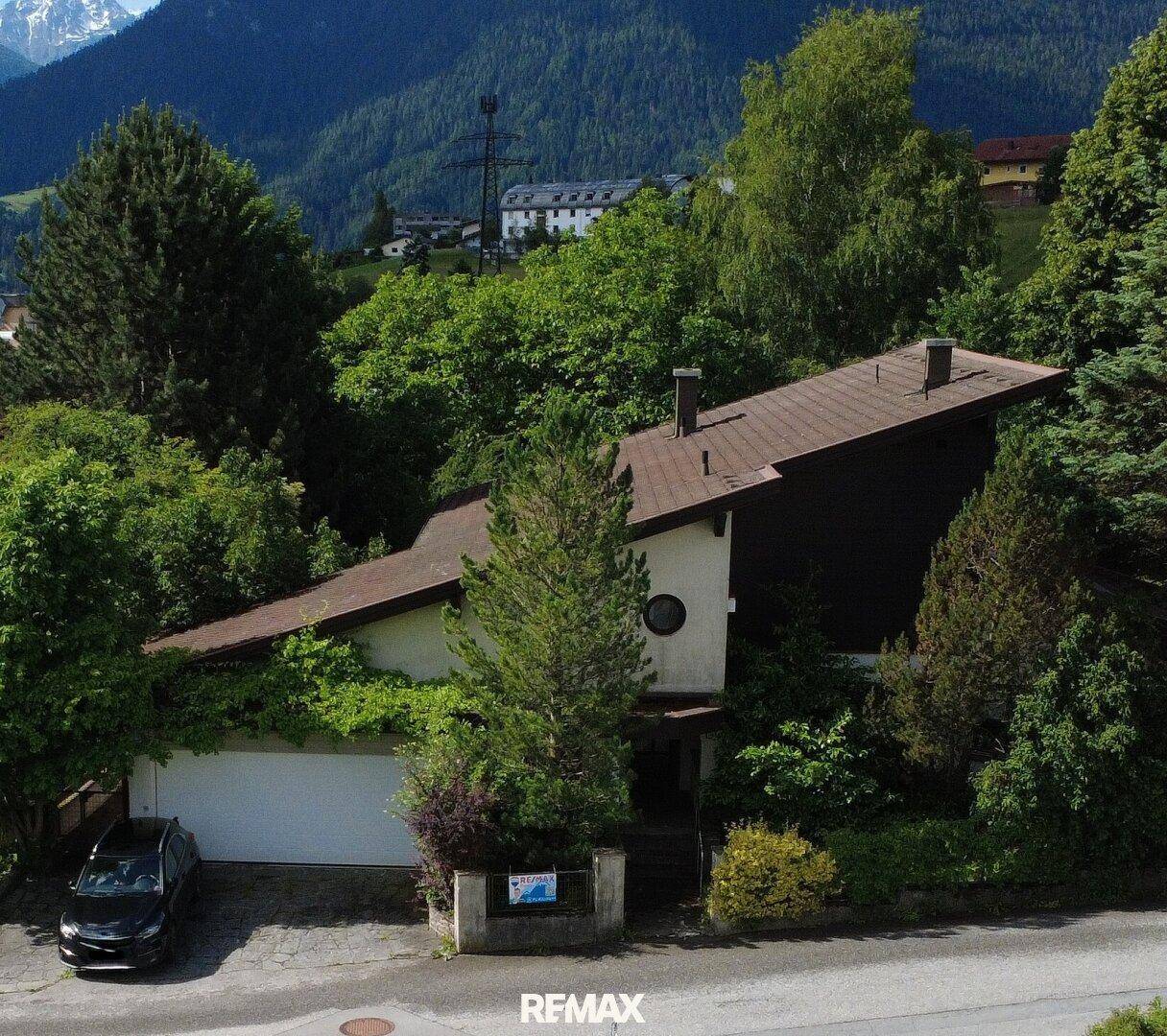 Freistehendes Haus mit Satteldach, umgeben von Bäumen und Bergblick im Hintergrund.