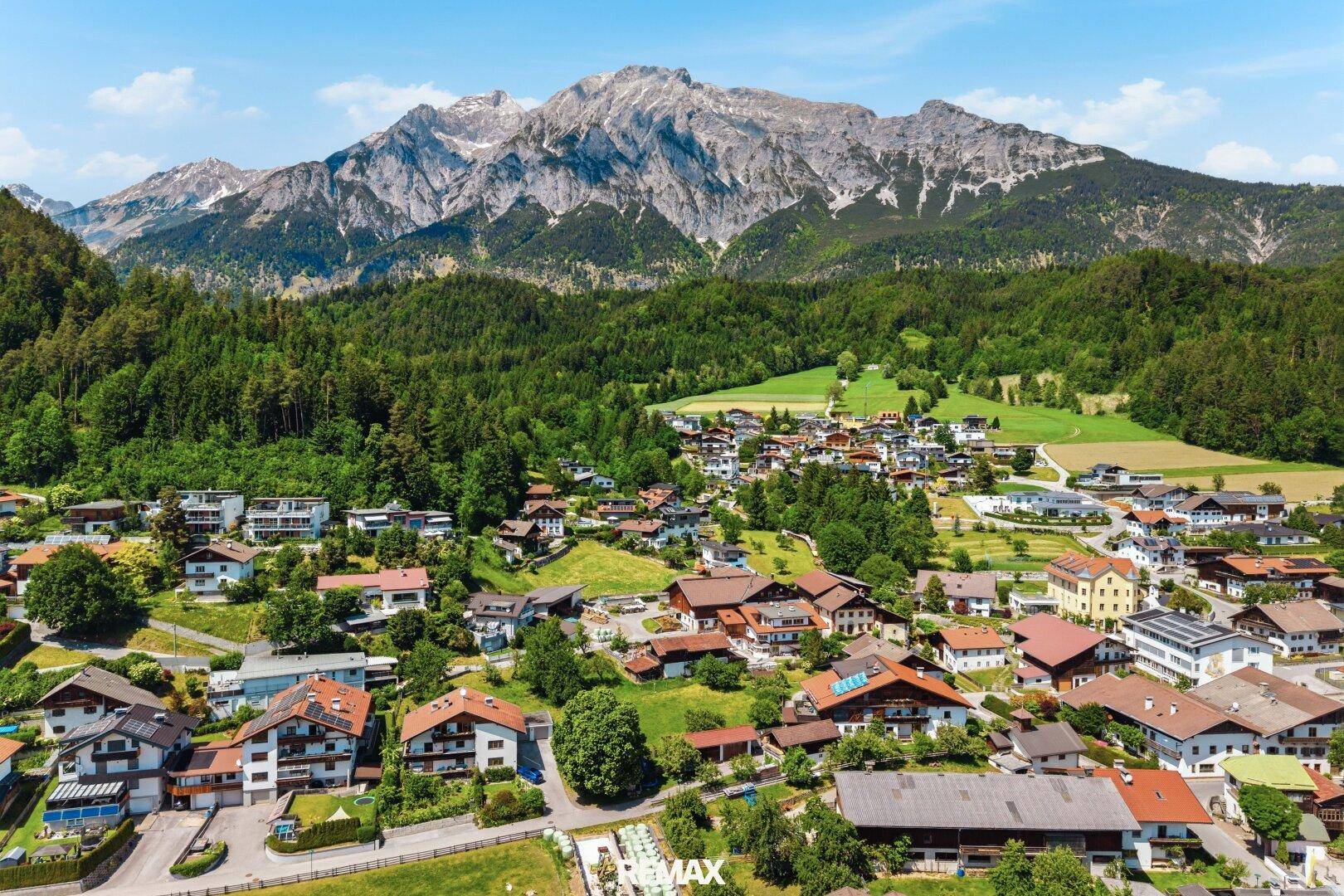 Panoramablick auf ein malerisches Dorf im Tal, umgeben von majestätischen Bergen und dichten Wäldern.