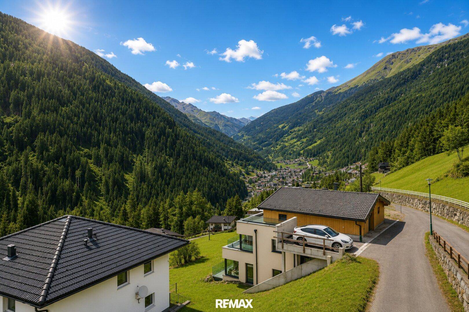 Panoramablick auf ein modernes Gebäude in einem grünen Tal mit bewaldeten Bergen.