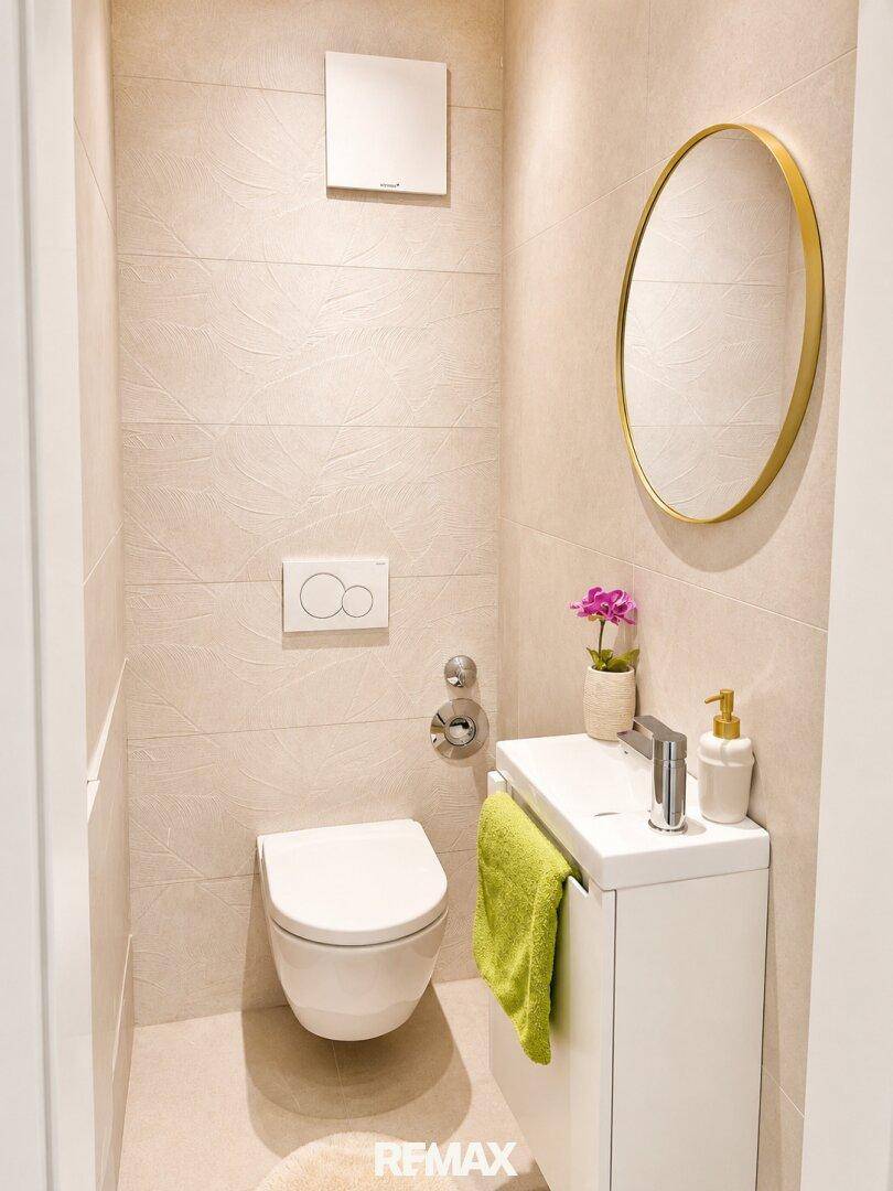 Kleines Gäste-WC mit wandhängender Toilette, modernem Waschbecken und rundem Spiegel.
