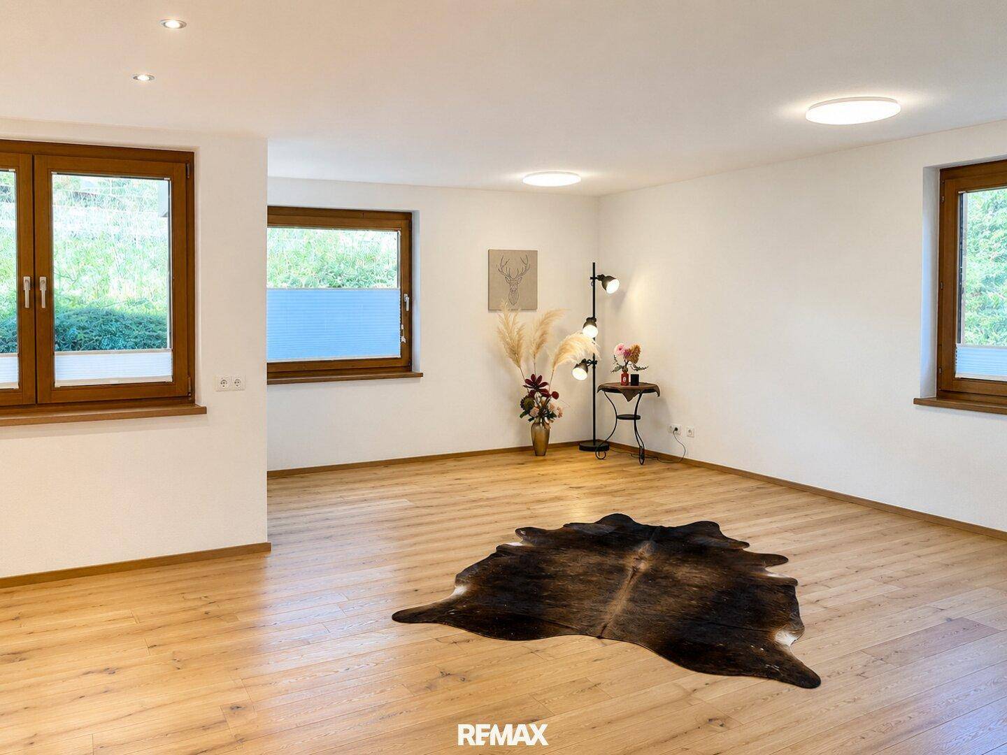 Helles Wohnzimmer mit Holzboden, großen Fenstern und einem dekorativen Teppich.