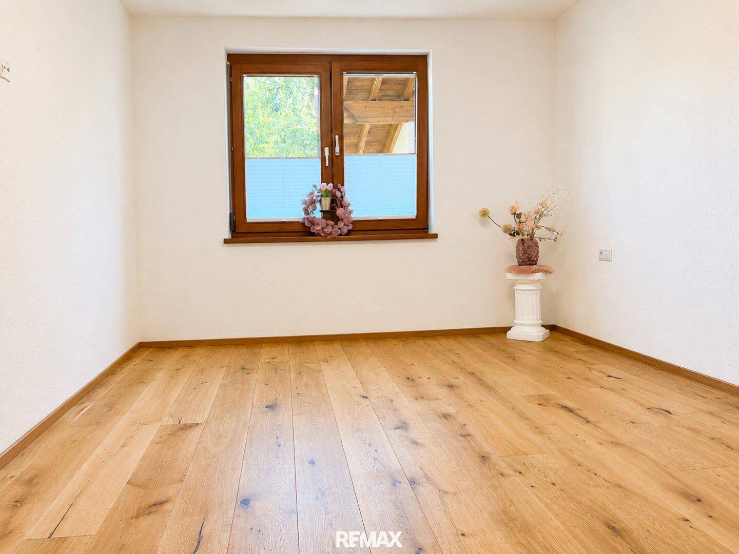 Helles Zimmer mit Holzboden und einem Fenster, das viel Tageslicht hereinlässt.