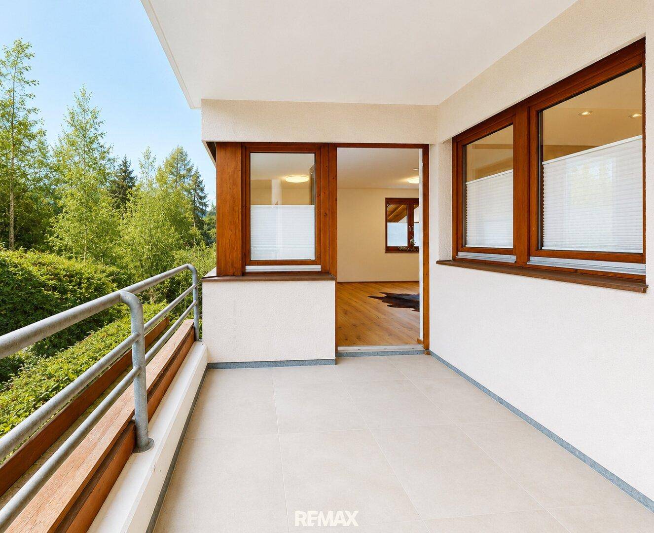 Heller Balkon mit Fliesenboden und Zugang zu einem Innenraum, umgeben von viel Grün.
