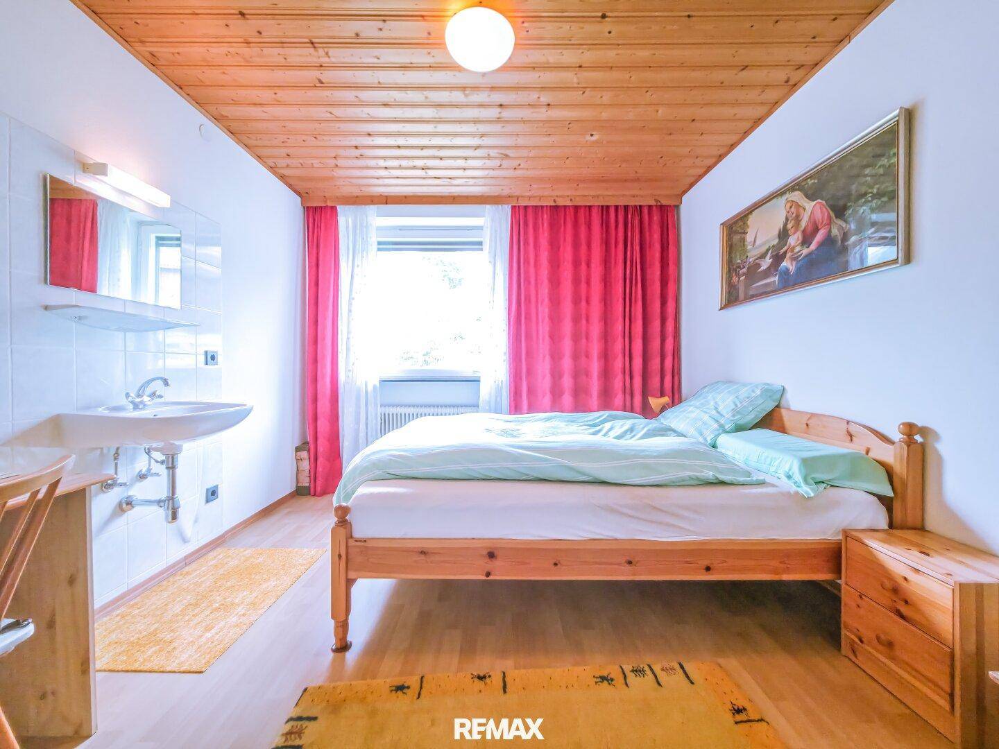 Schlafzimmer mit Holzdecke, Parkettboden und integriertem Waschbeckenbereich.