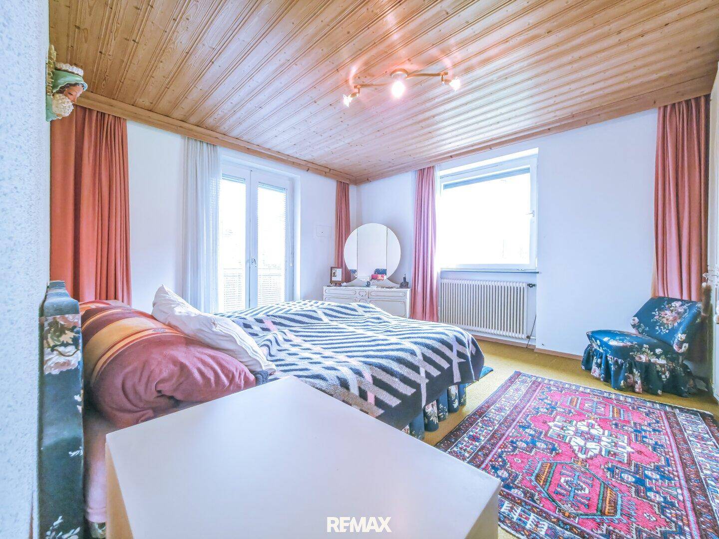 Schlafzimmer mit Holzbalkendecke, Teppichboden und Zugang zu einem Balkon.