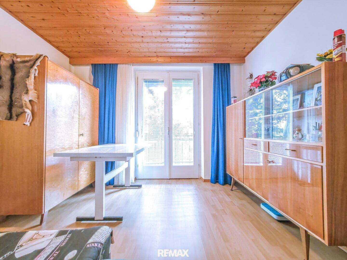 Helles Zimmer mit Holzdecke, Parkettboden und Zugang zu einem französischen Balkon.