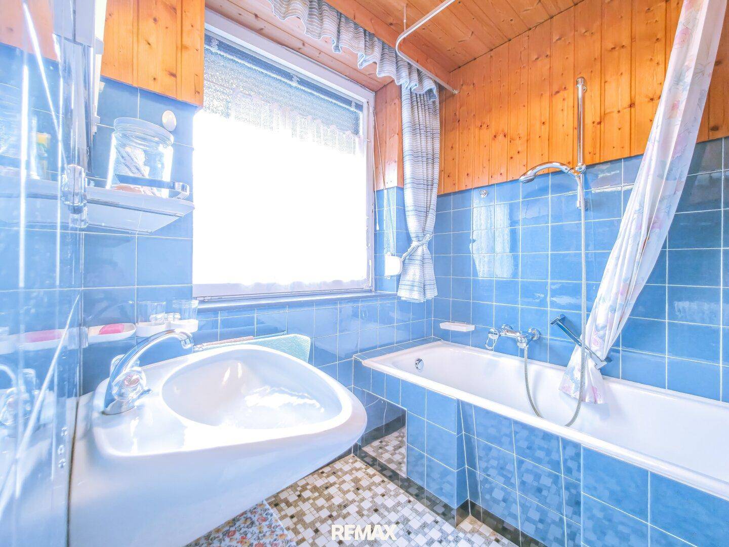 Badezimmer mit blauen Fliesen, Badewanne und Waschbecken, sowie Holzdecke.