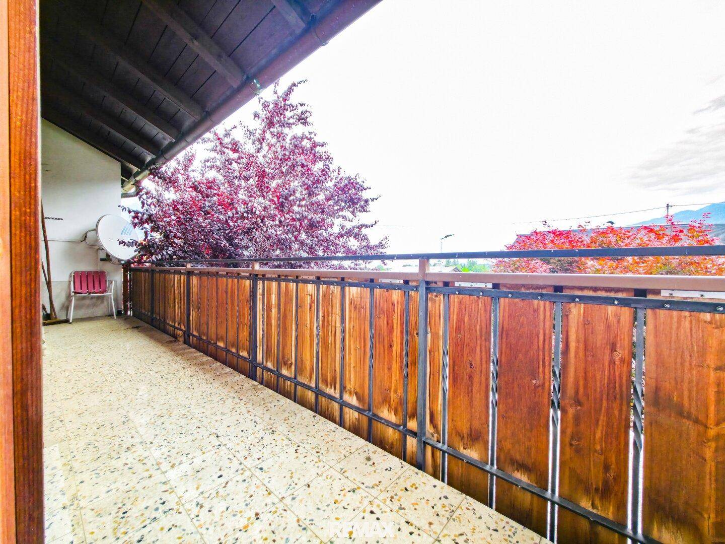 Langer Balkon mit Holzgeländer und Fliesenboden, bietet einen Blick auf die Umgebung.