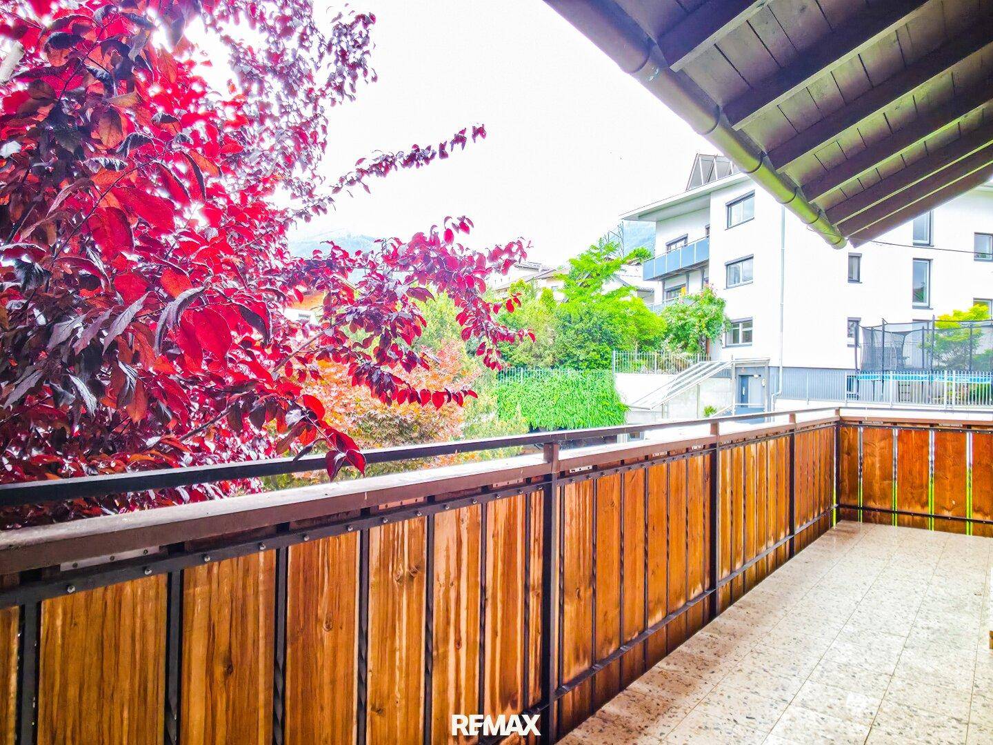 Balkon mit Holzgeländer und Blick auf die umliegende Bebauung und grüne Landschaft.