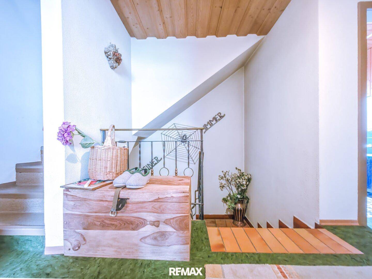 Eingangsbereich mit Treppe, Holztruhe und grünem Teppichboden, der nach oben führt.
