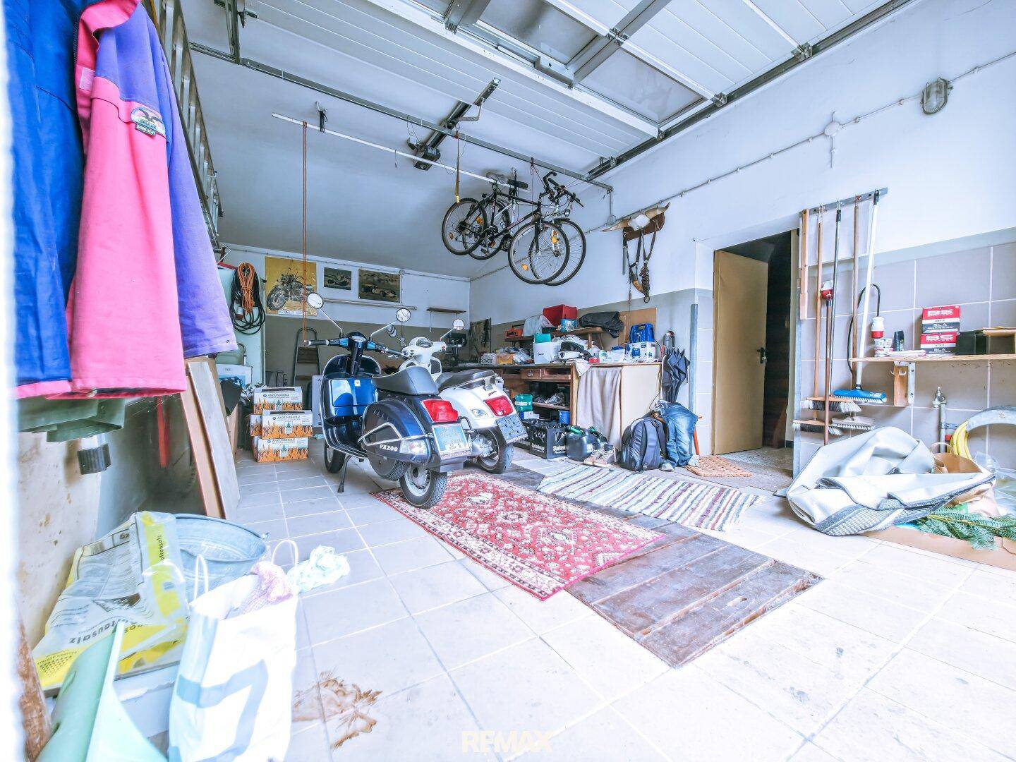 Geräumige Garage mit Fliesenboden, Stauraum und Platz für Fahrzeuge sowie Fahrräder.