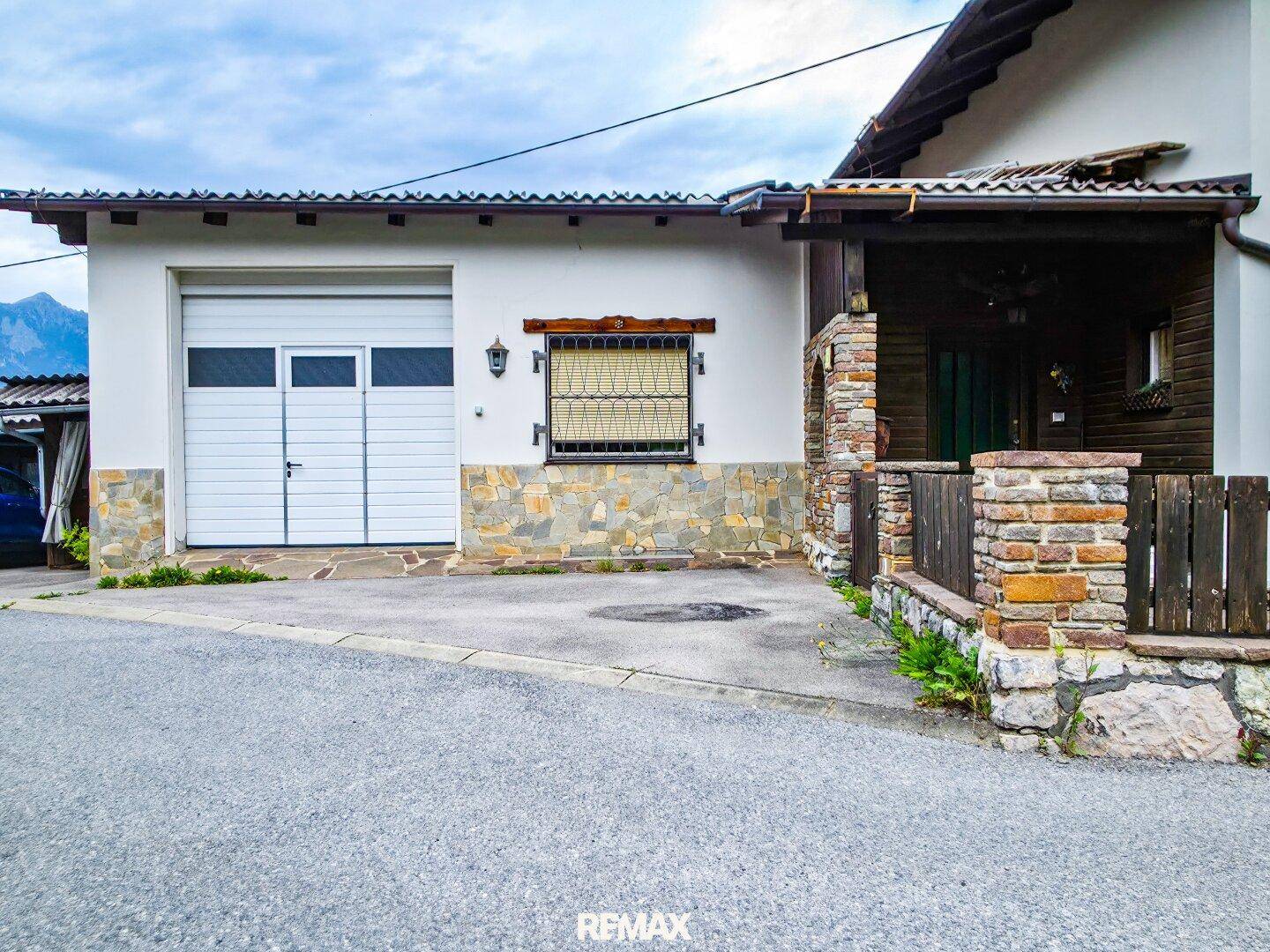 Außenansicht des Hauses mit Garage und Steinfassade, umgeben von einer gepflasterten Zufahrt.
