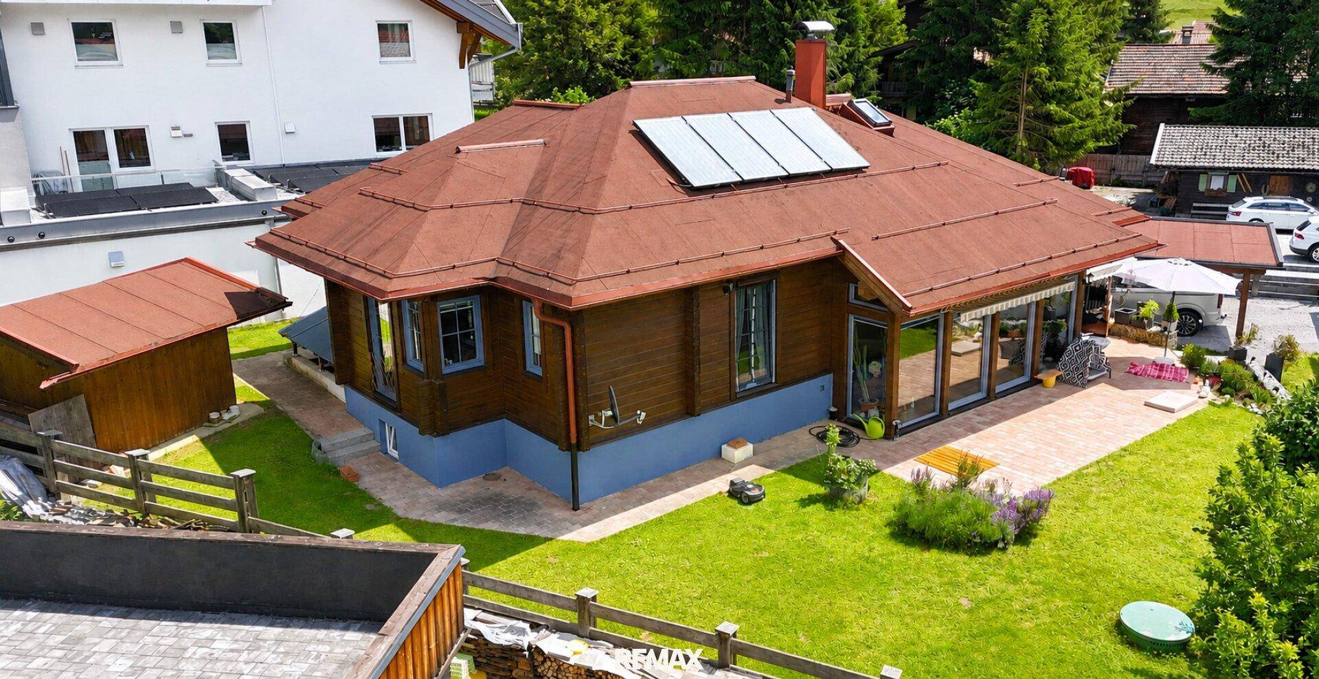Charmantes Holzhaus mit rotem Dach, Solarpaneelen und gepflegtem Garten in alpiner Umgebung.