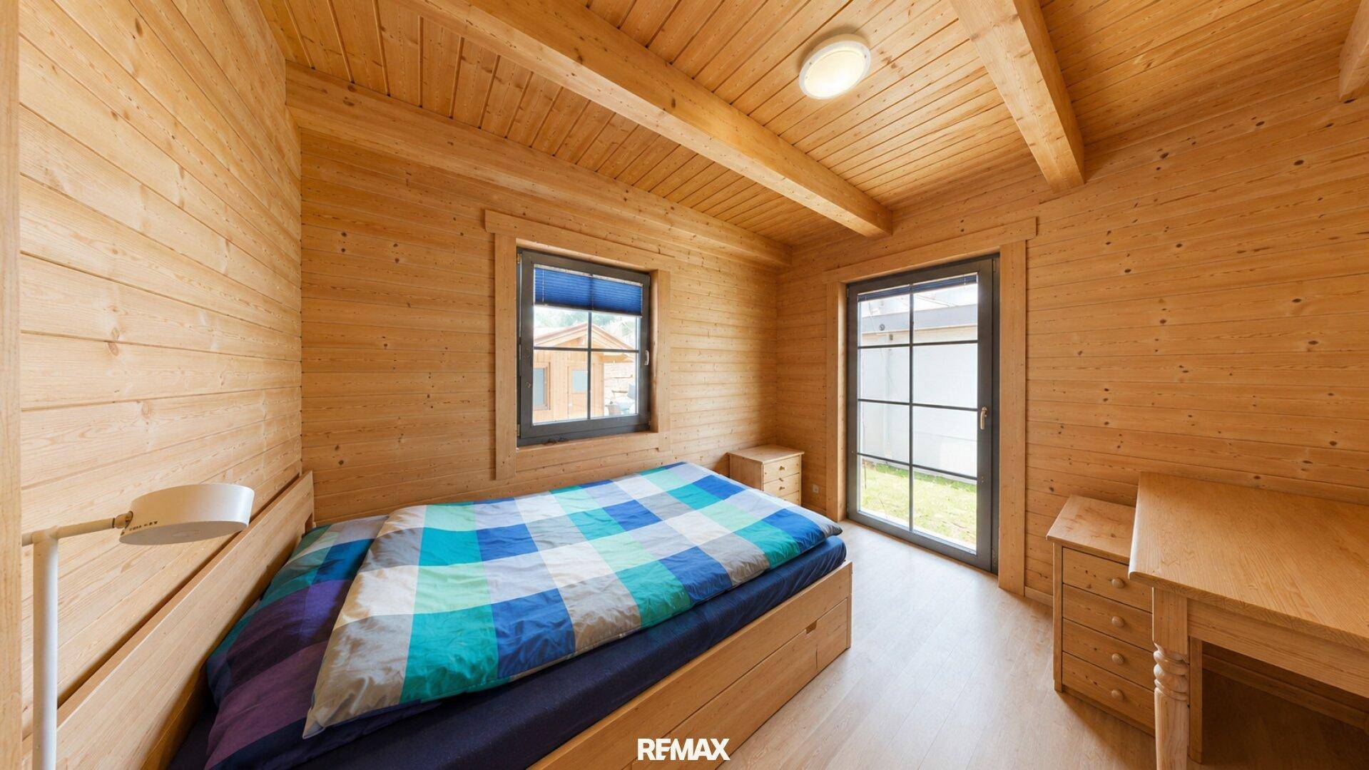 Gemütliches Schlafzimmer mit Holzwänden, Holzbalkendecke und einem Fenster mit Blick ins Grüne.