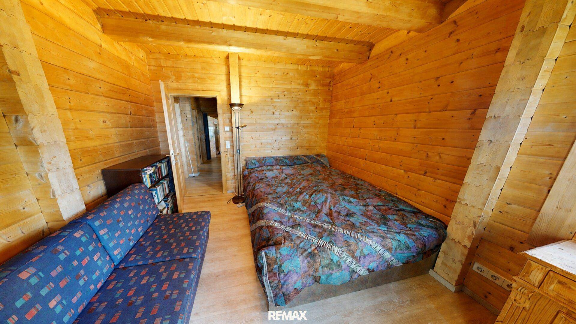 Schlafzimmer mit Holzwänden, Holzbalkendecke und einem gemütlichen Sofa.