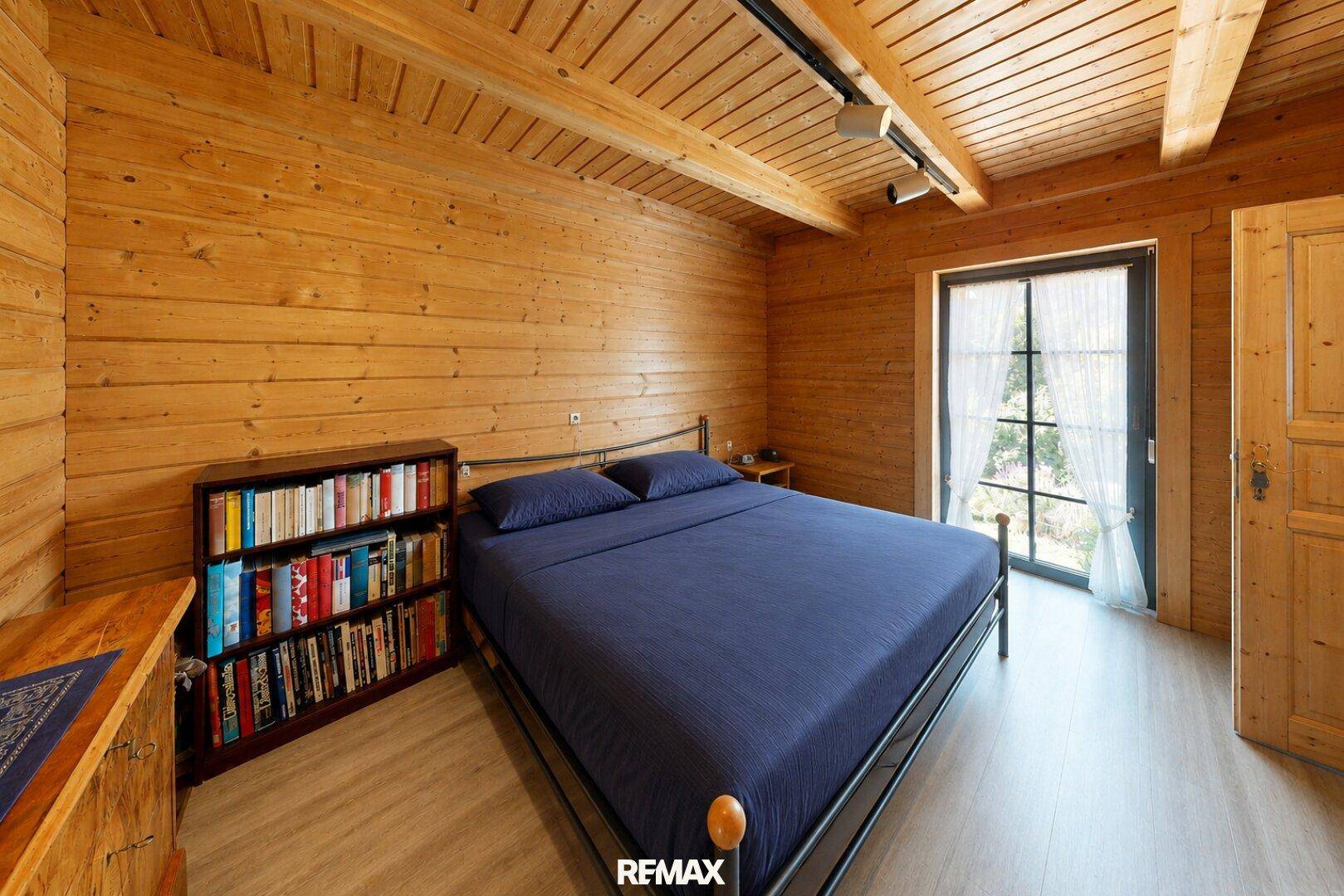 Schlafzimmer mit Holzwänden, Holzbalkendecke und Zugang zu einem Außenbereich.