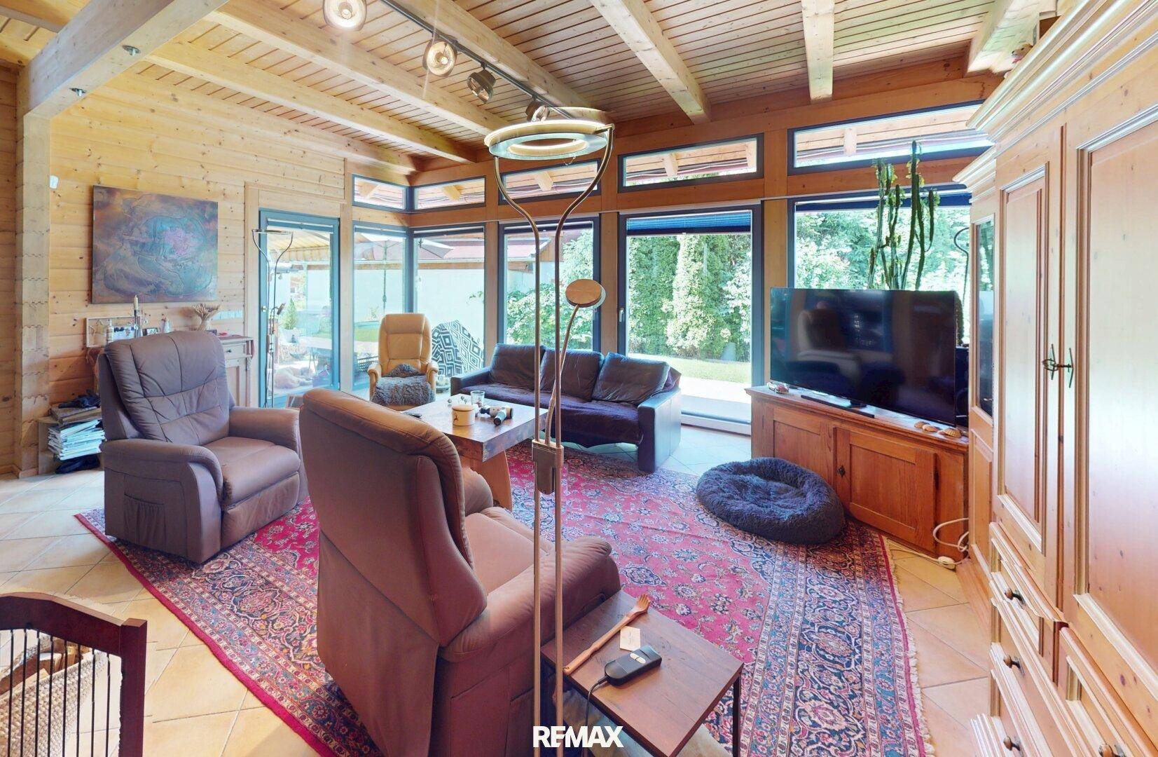Helles Wohnzimmer mit Holzbalkendecke, großen Fenstern und Blick in den Garten.