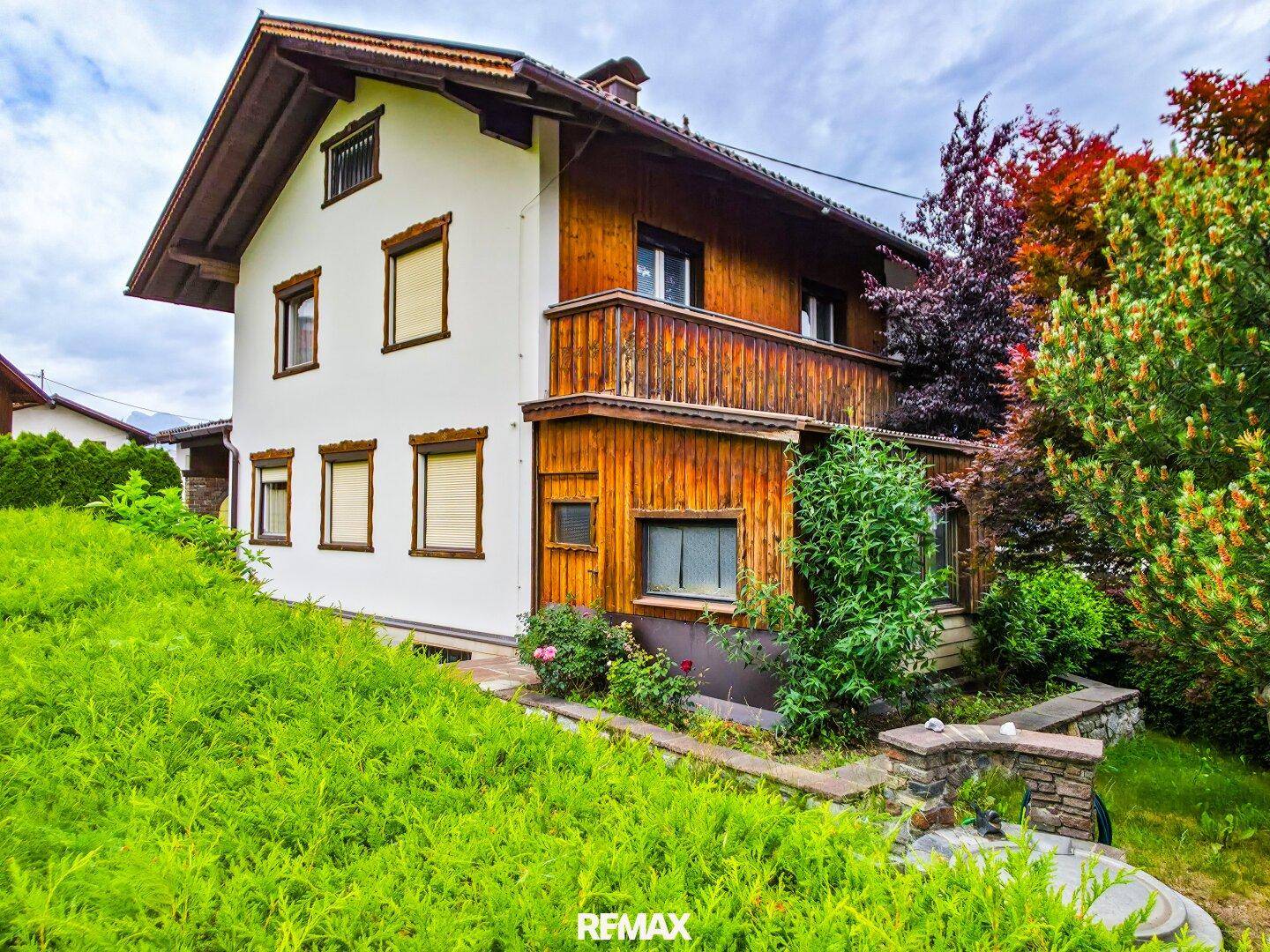 Seitenansicht des Hauses mit weißer Fassade, Holzverkleidung und einem terrassierten Gartenbereich.