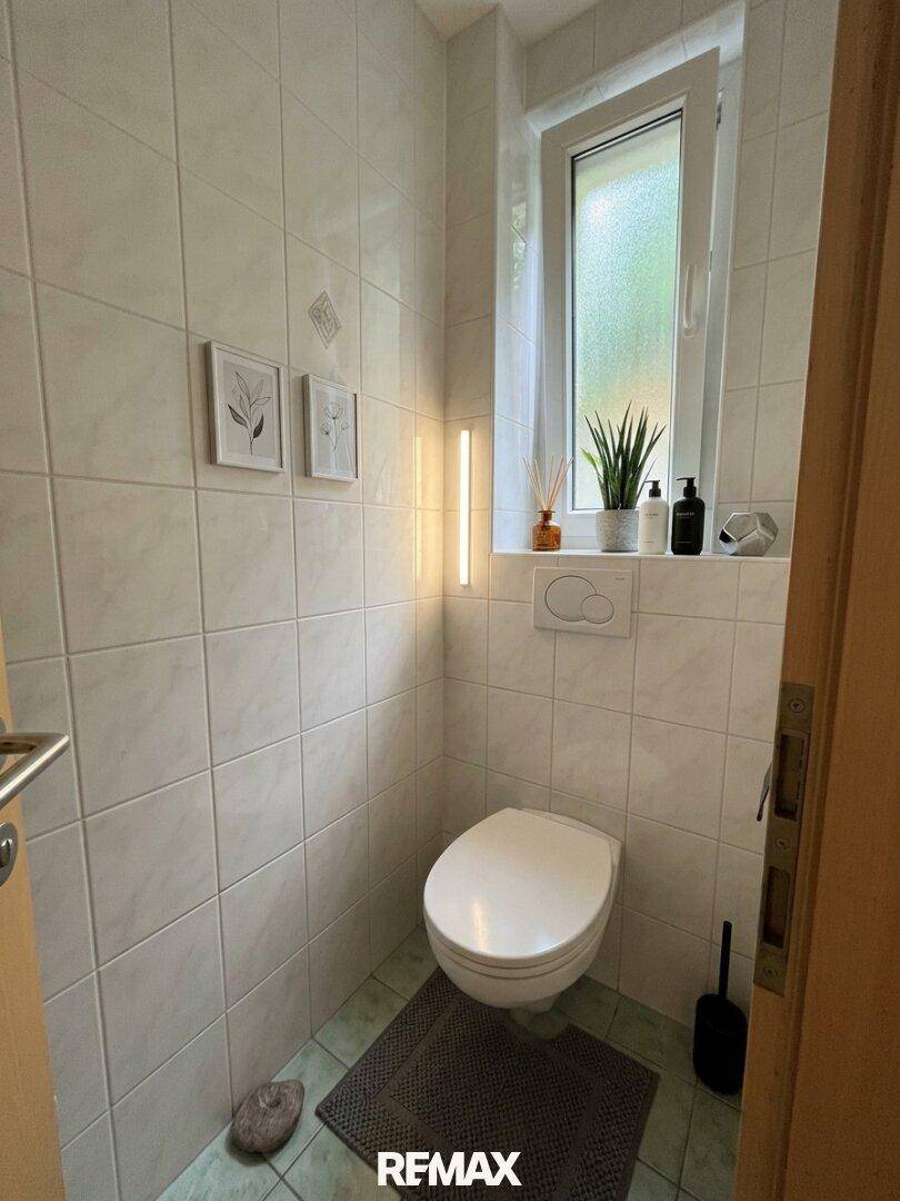 Separates WC mit Fenster, Wand-WC und Fliesenboden in hellem Design.