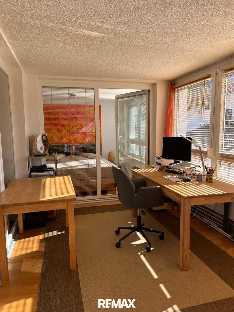 Helles Büro mit Holztischen und Blick in ein angrenzendes Schlafzimmer, durchflutet von Sonnenlicht.