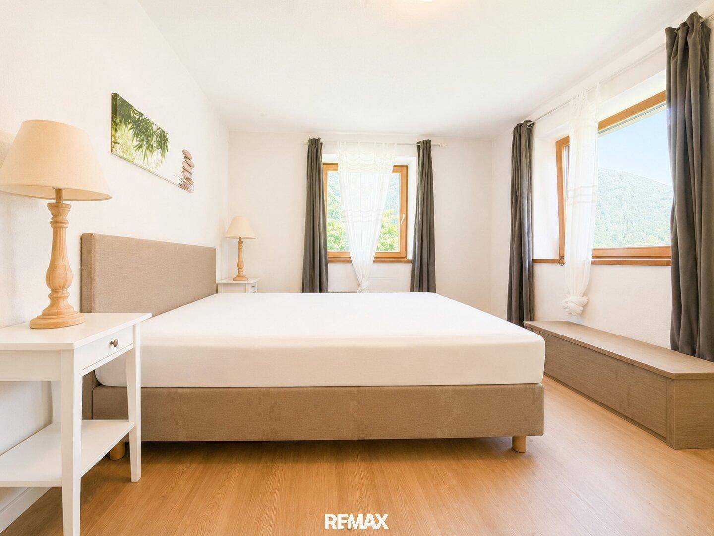 Geräumiges Schlafzimmer mit Doppelbett, Holzboden und zwei Fenstern für viel Licht.