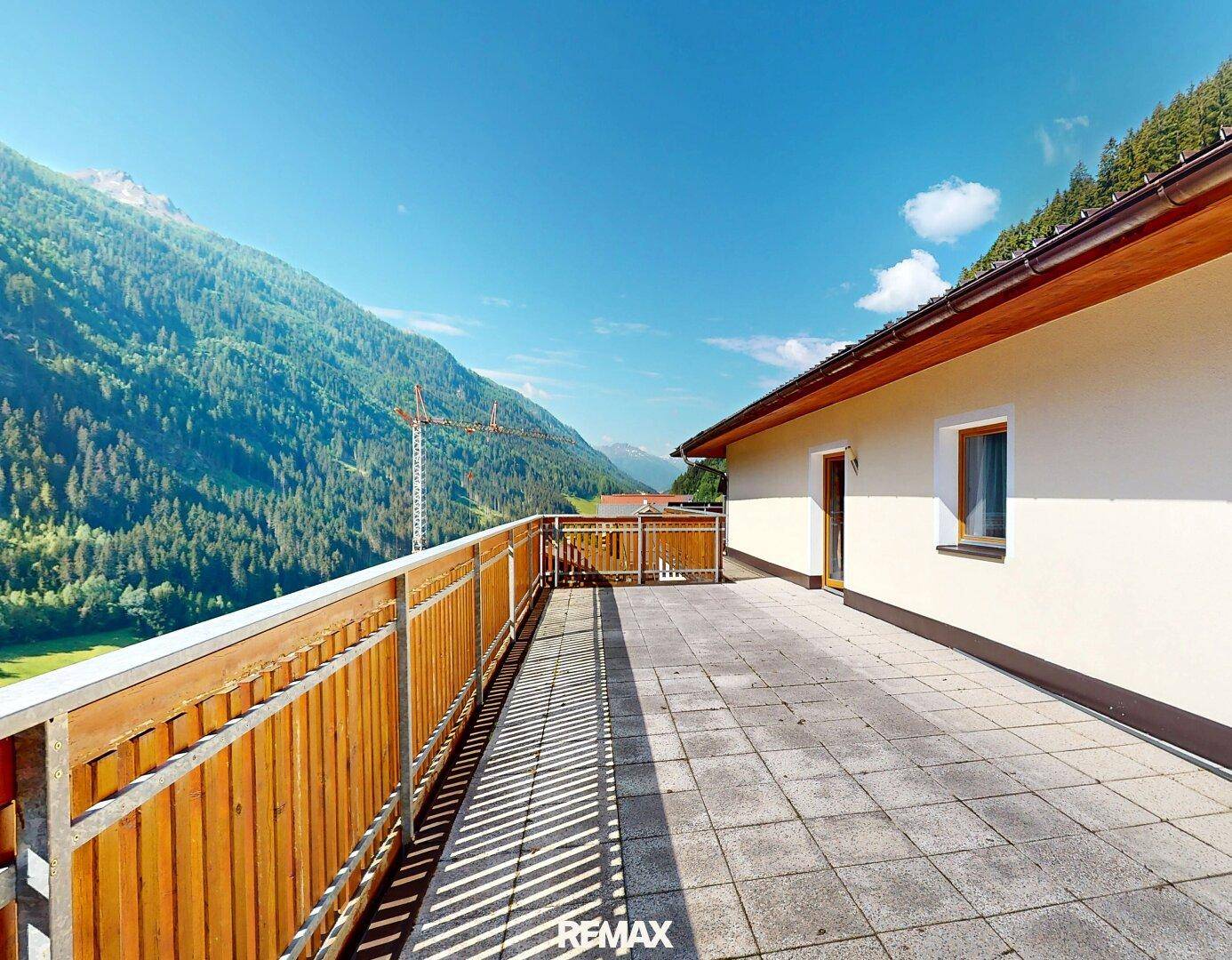 Geräumige Terrasse mit Steinplatten und Holzgeländer, bietet einen weiten Blick auf die umliegenden Berge.