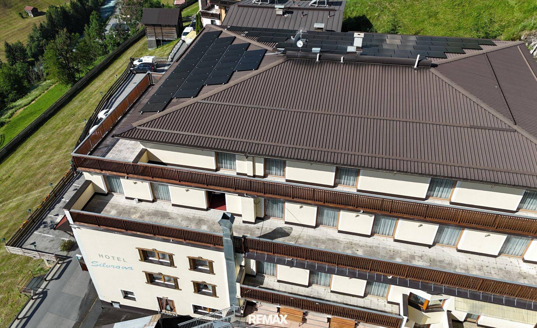 Dachansicht des Hotels mit Solarpaneelen und umliegender Berglandschaft unter blauem Himmel.