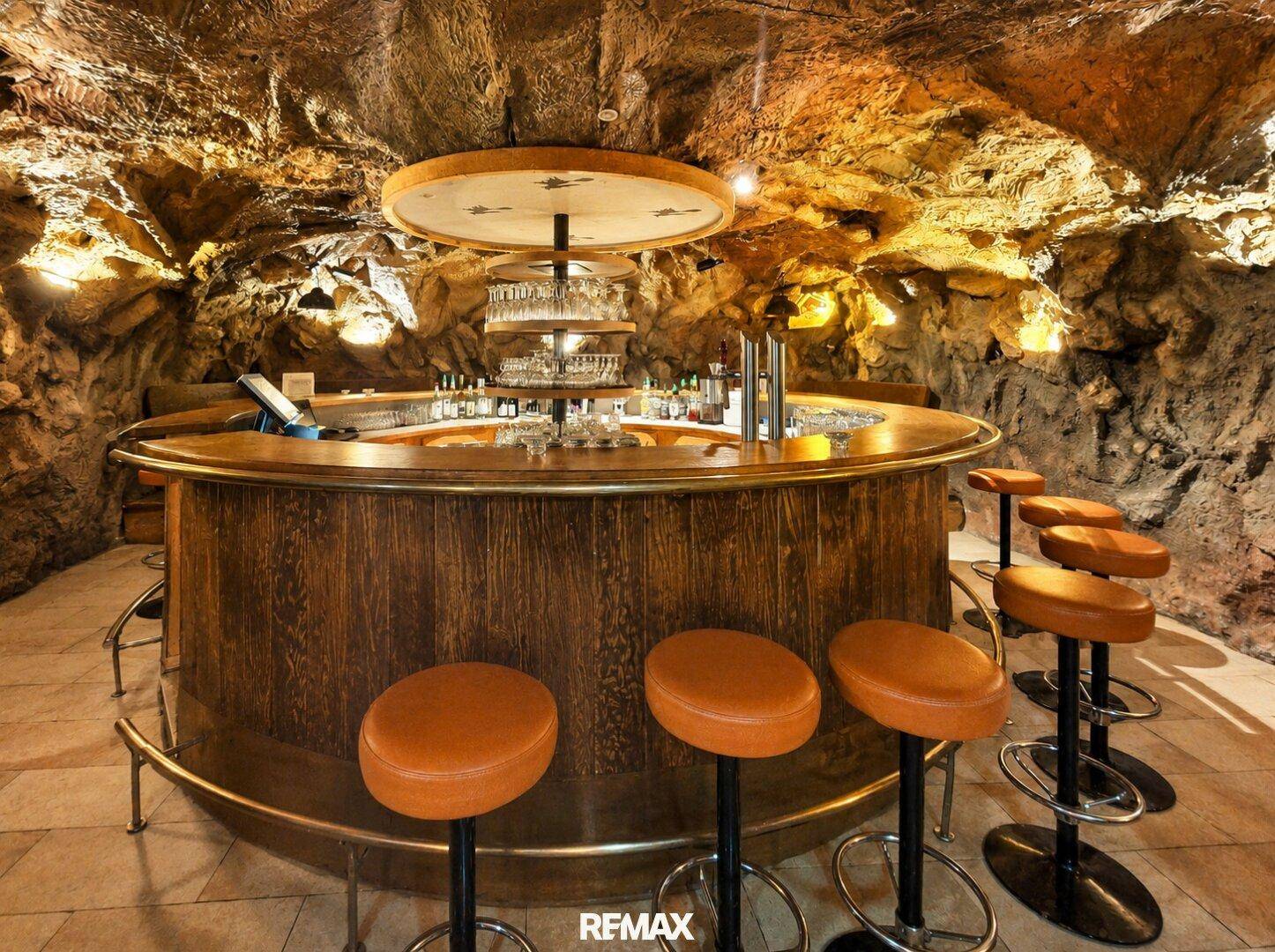 Einzigartige Bar in Höhlenoptik mit runder Holztheke und Hockern, stimmungsvoll beleuchtet.