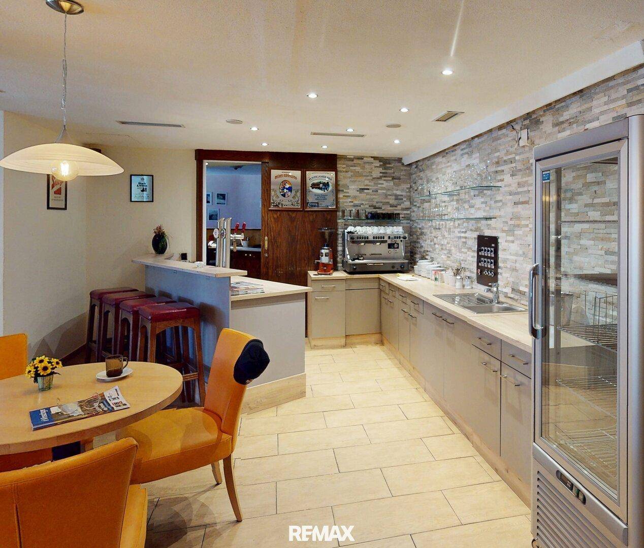Moderne Bar mit Steinfliesenwand, Kaffeemaschine und Kühlschrank, daneben ein kleiner Essbereich.