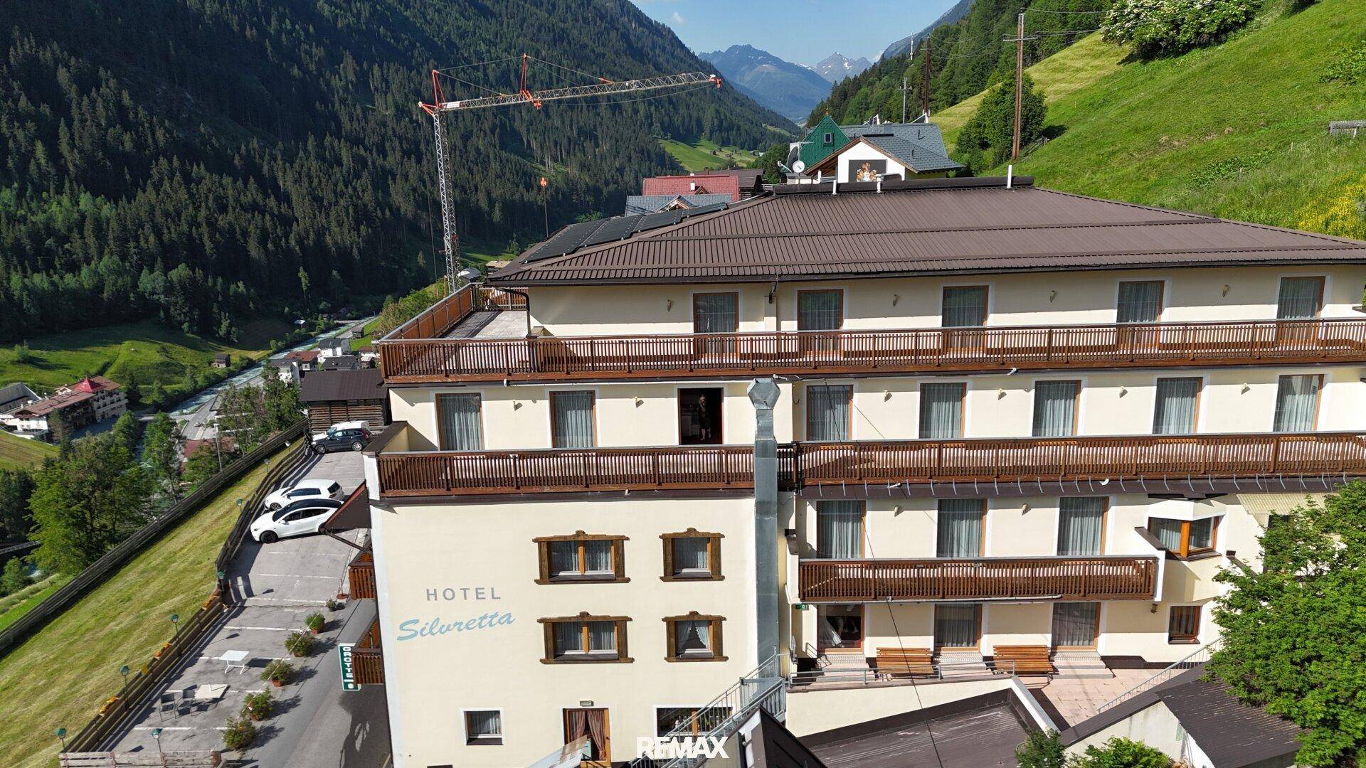 Hotelgebäude in alpiner Umgebung mit Balkonen und Blick auf das Tal und die umliegenden Berge.