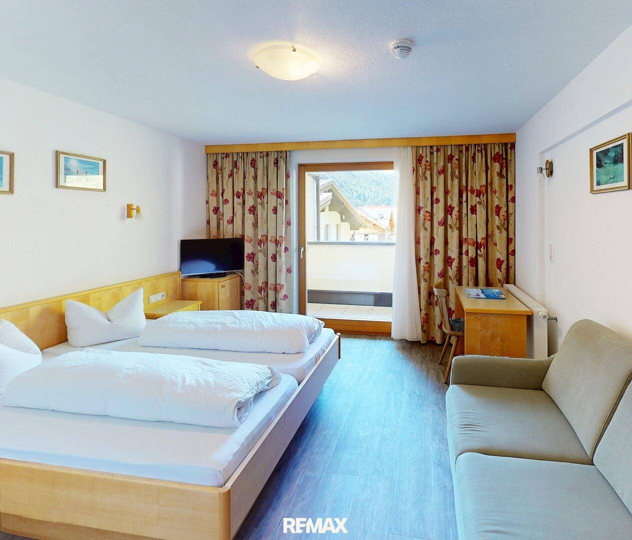 Gemütliches Schlafzimmer mit zwei Einzelbetten, Schreibtisch und Zugang zu einem kleinen Balkon.