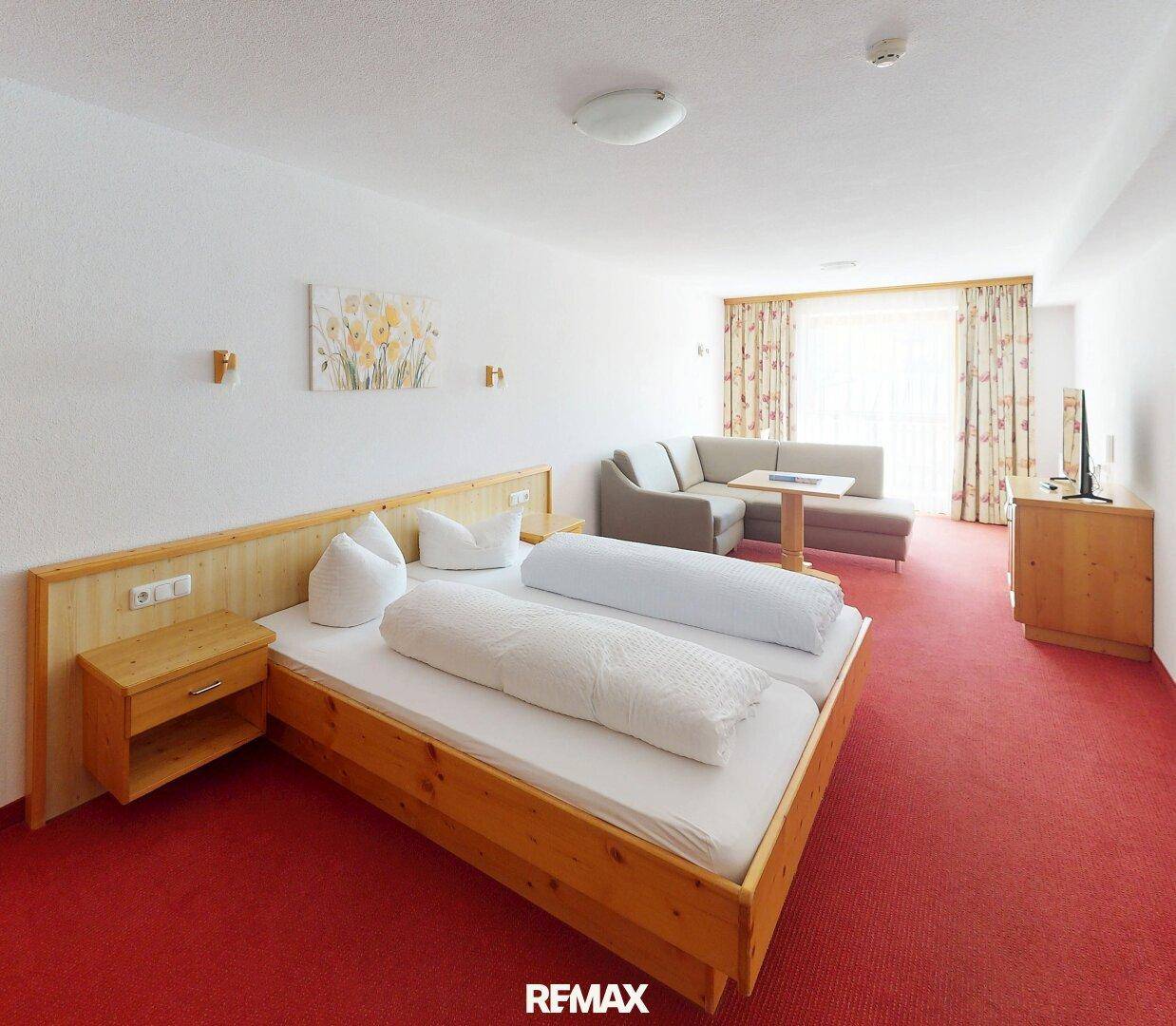 Geräumiges Schlafzimmer mit Doppelbett, rotem Teppichboden und Sofa, bietet Komfort und Platz.