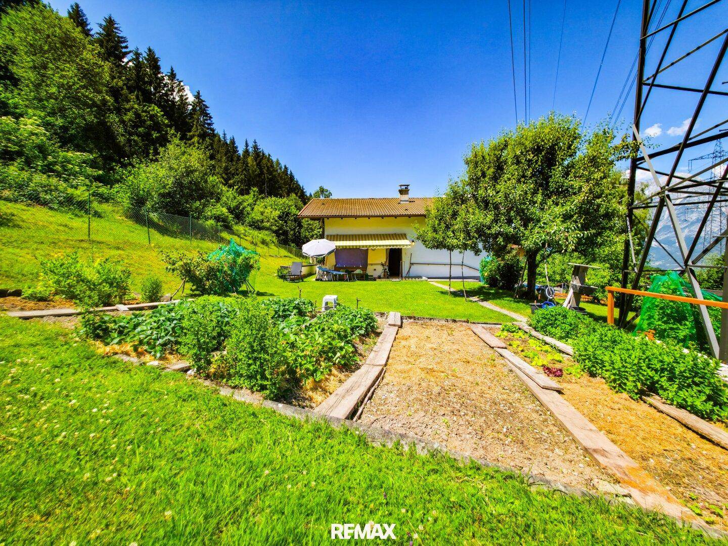 Hinteransicht des Hauses mit großem Garten, Hochbeeten und einer gemütlichen Sitzecke im Freien.