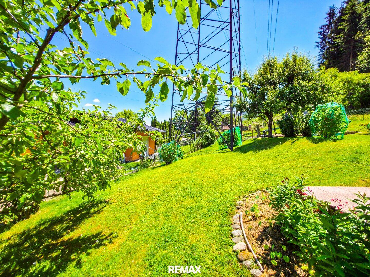Großer Gartenbereich mit Rasenflächen, Bäumen und einem markanten Strommast im Hintergrund.
