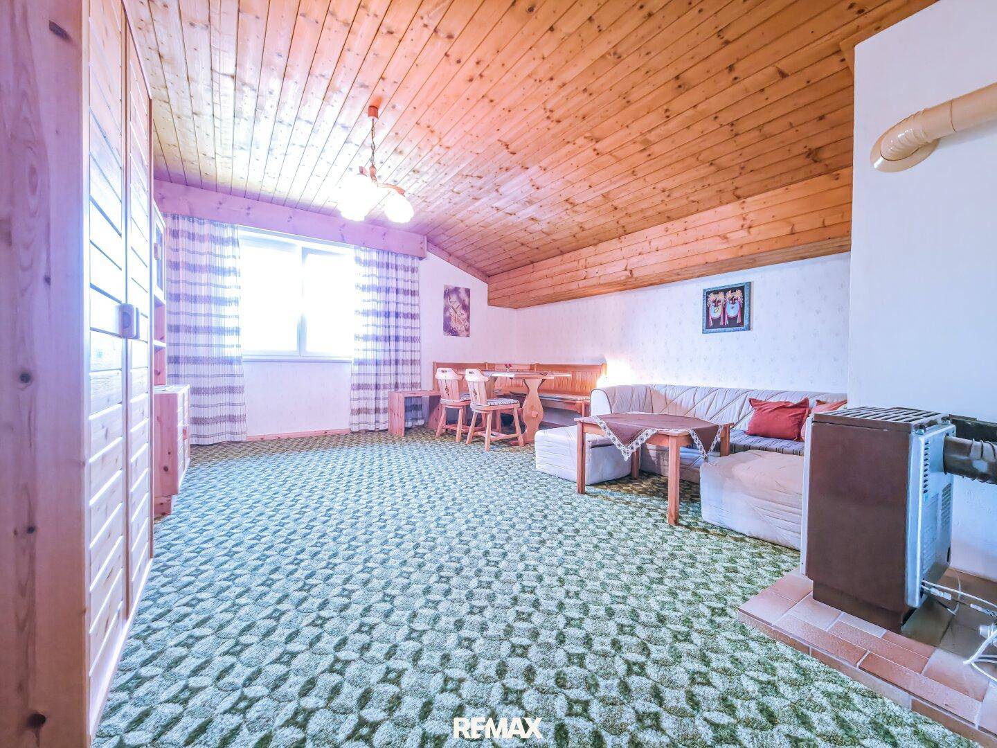 Geräumiges Wohnzimmer mit Holzdecke, Teppichboden und einem gemütlichen Holzofen.