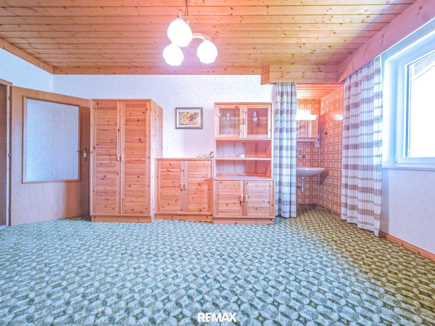 Schlafzimmer mit Holzmöbeln, Teppichboden und einer kleinen Waschecke unter der Dachschräge.