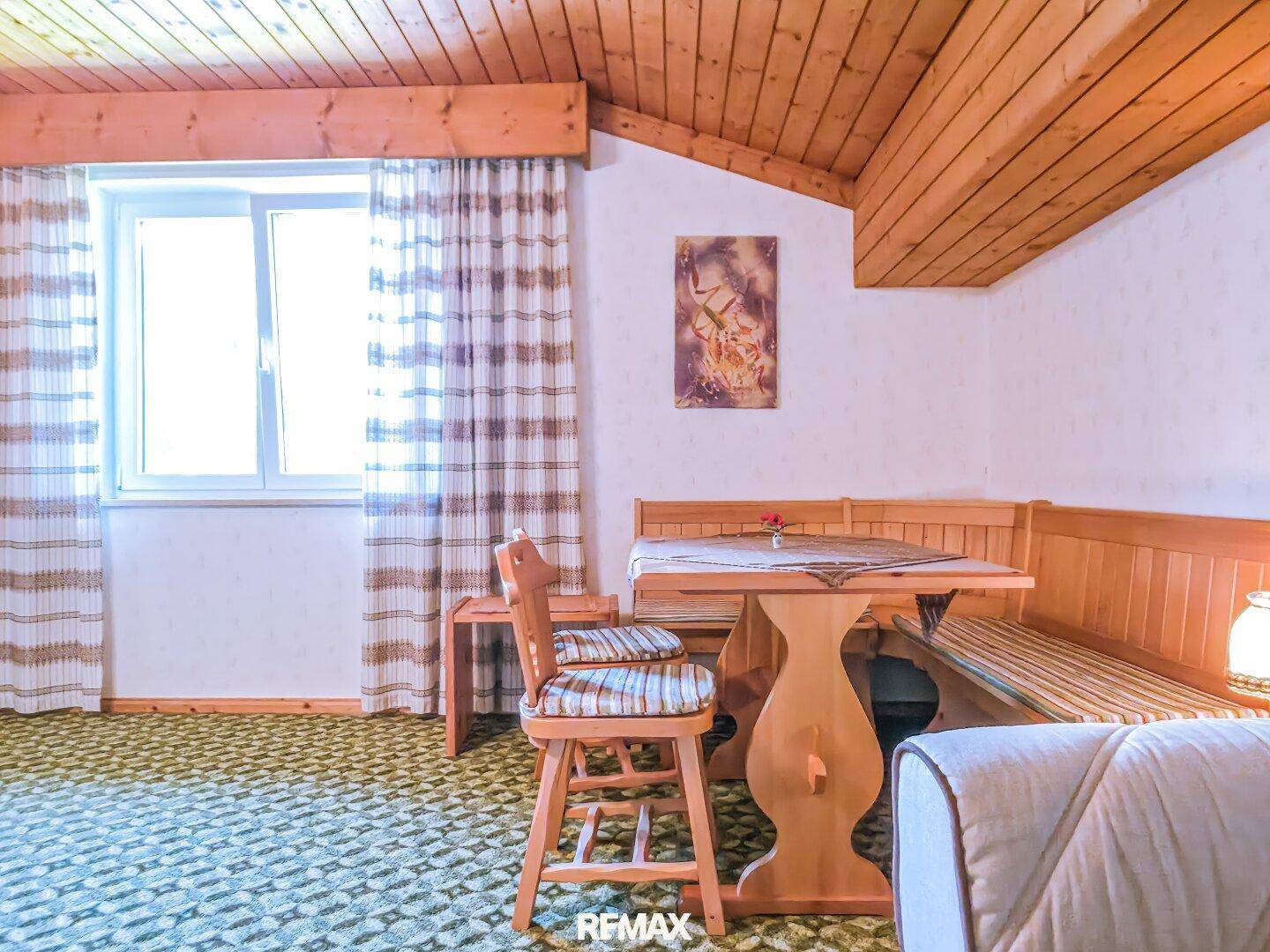 Essbereich in einem Zimmer mit Holzdecke, Teppichboden und einem großen Fenster.