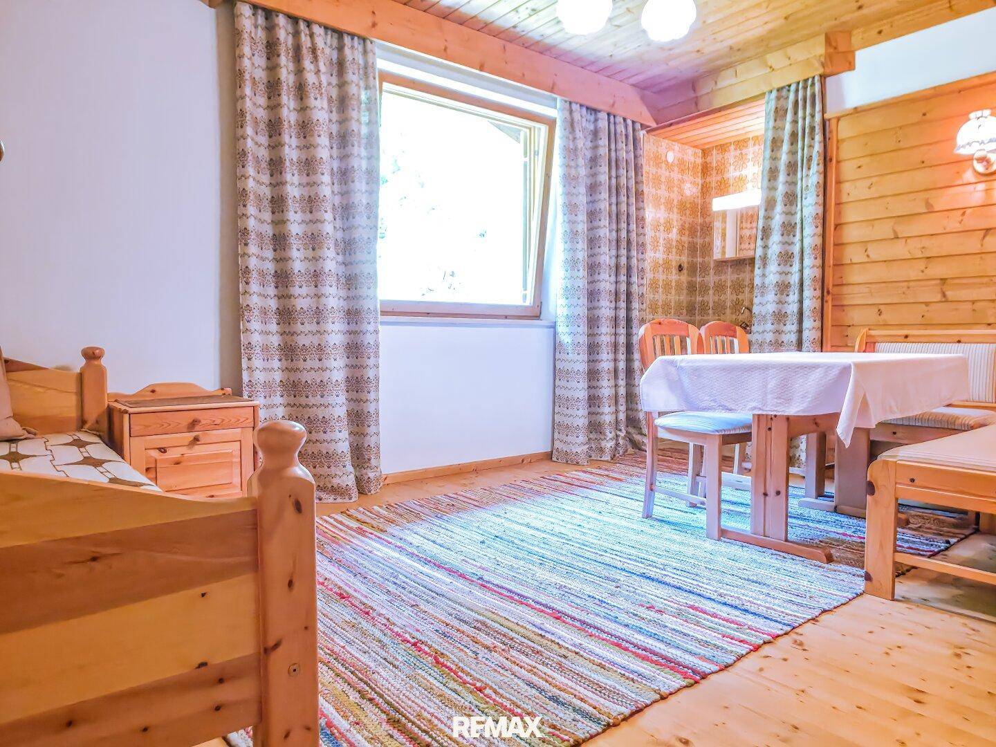 Schlafzimmer mit Holzbett, Holzboden und einem Esstisch, akzentuiert durch bunte Teppiche.