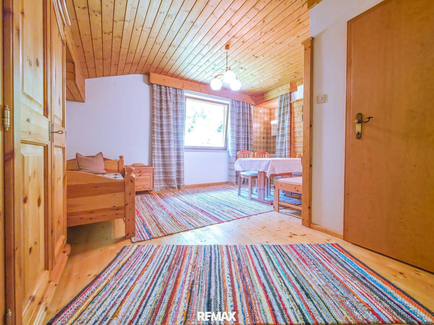 Helles Schlafzimmer mit Holzboden, traditionellen Möbeln und bunten Teppichen.