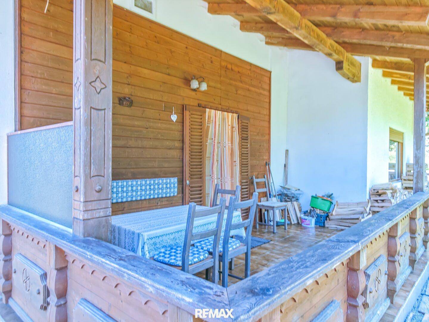 Überdachter Balkon mit Holzbalken, traditionellen Schnitzereien und Sitzgelegenheiten.