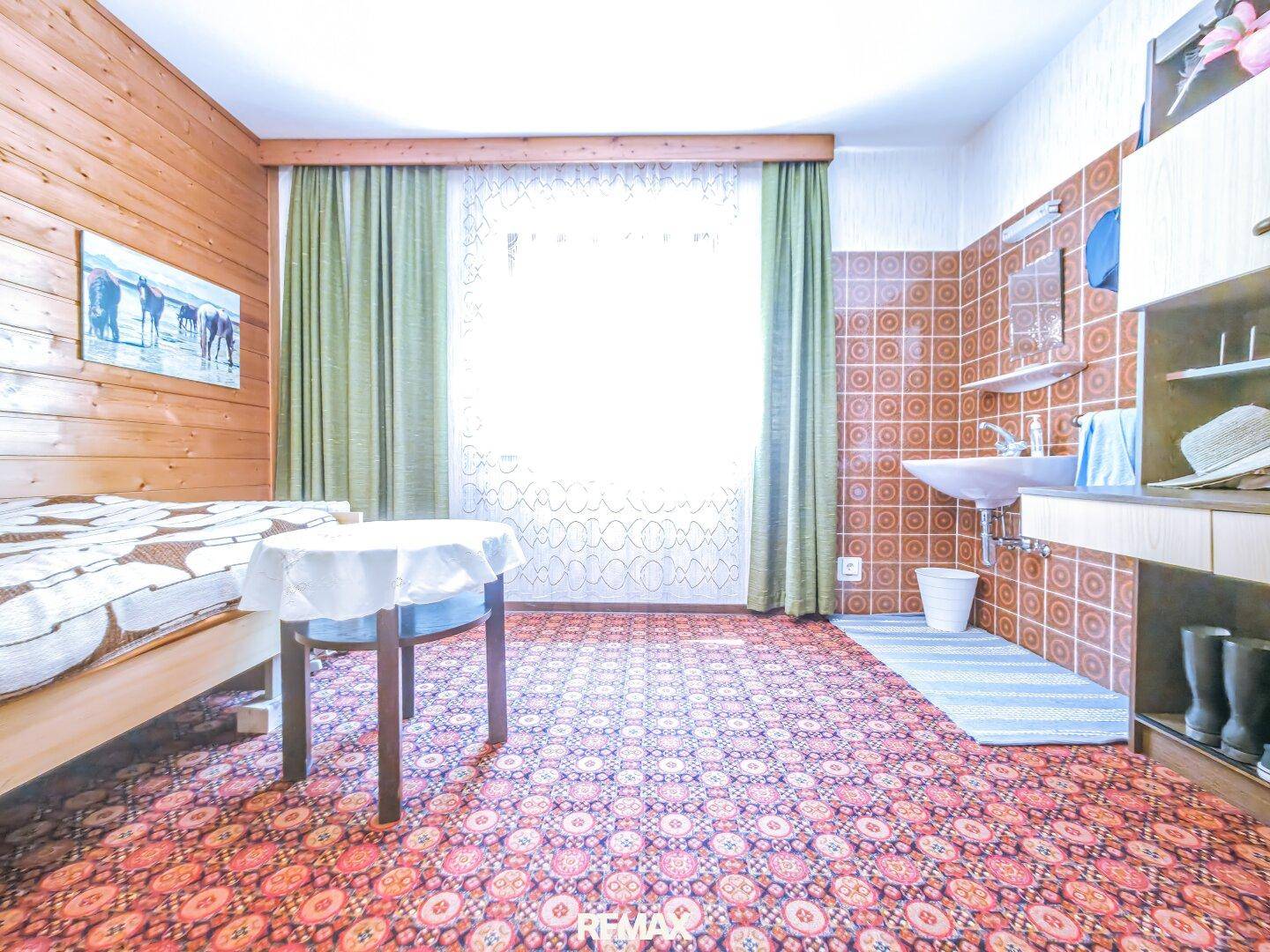 Schlafzimmer mit Holztäfelung, gemustertem Teppich, Bett und einem Waschbecken in der Ecke.