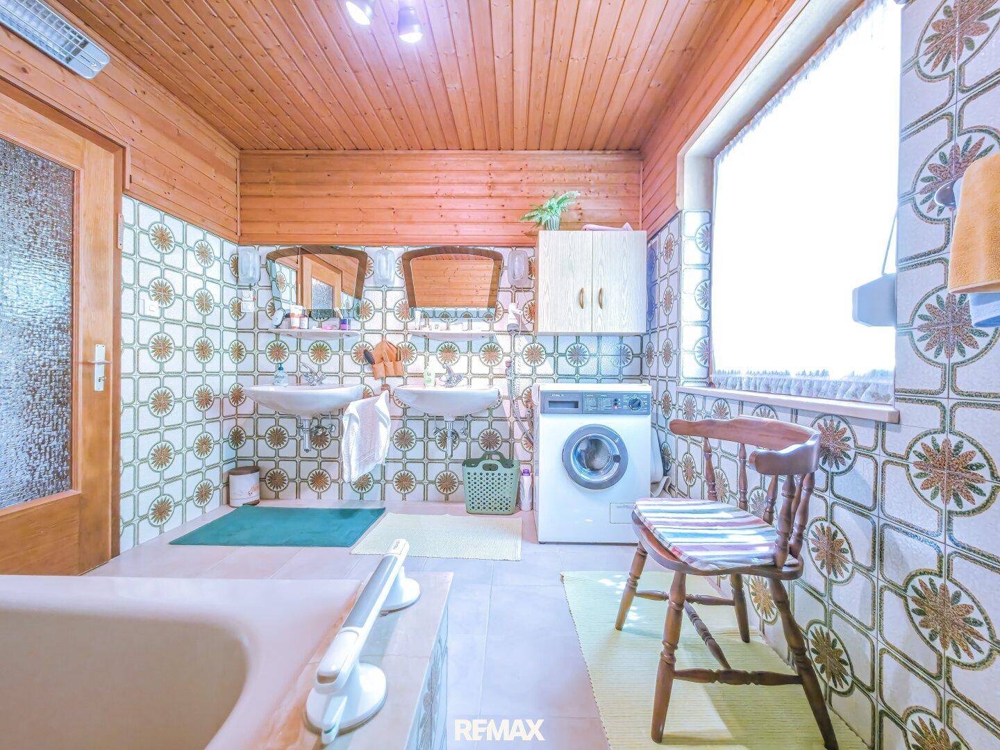 Badezimmer mit gemusterten Fliesen, Doppelwaschbecken, Waschmaschine und Fenster.