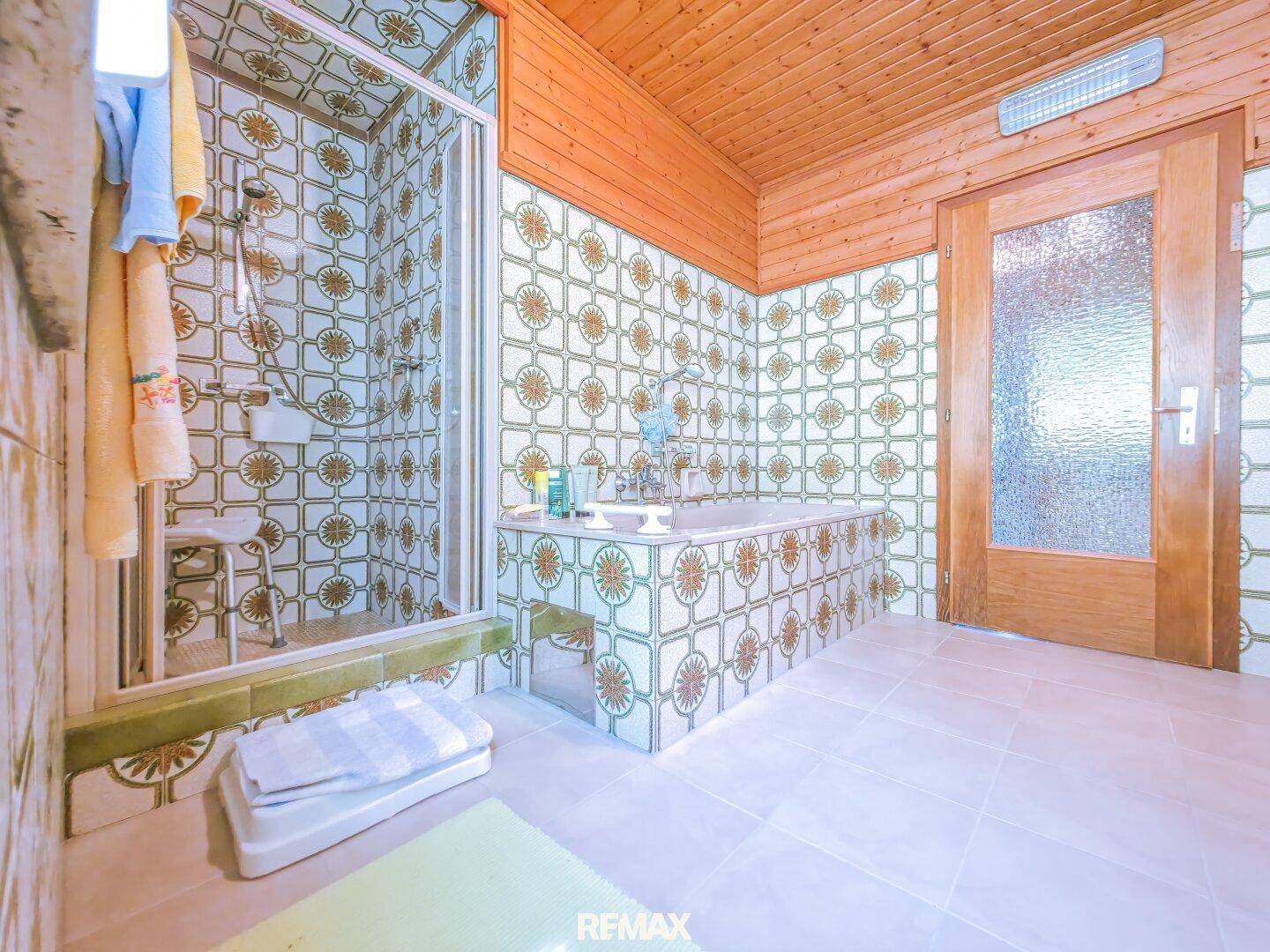 Badezimmer mit gemusterten Fliesen, Badewanne und Duschkabine unter einer Holzdecke.