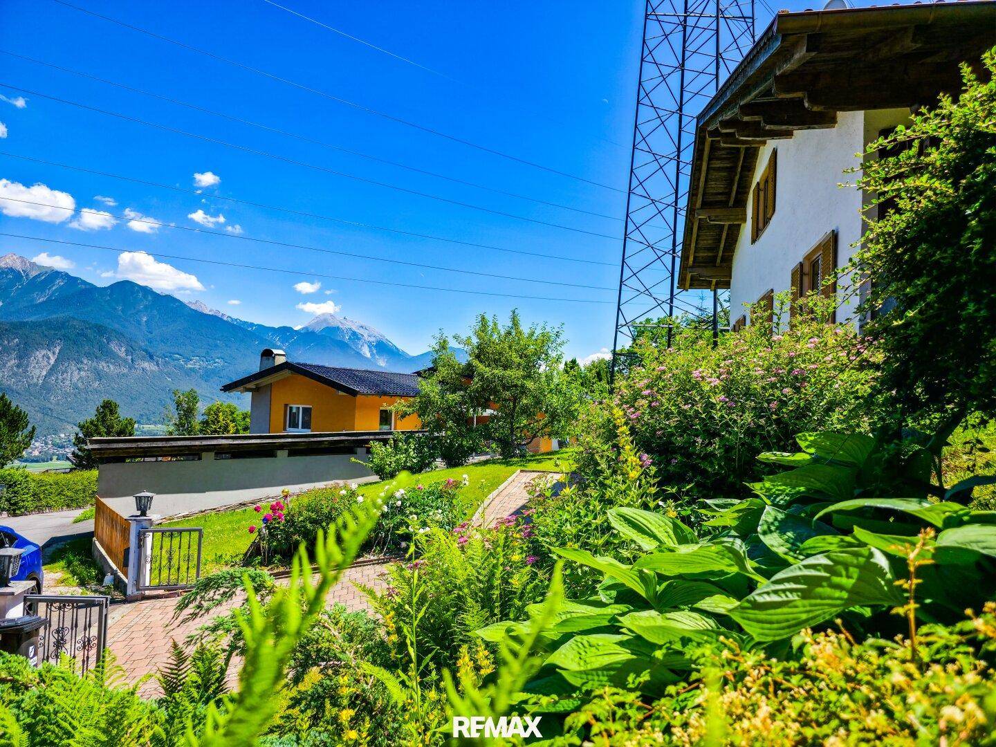 Gepflegter Gartenweg mit üppiger Bepflanzung und weitem Blick auf die umliegende Berglandschaft.