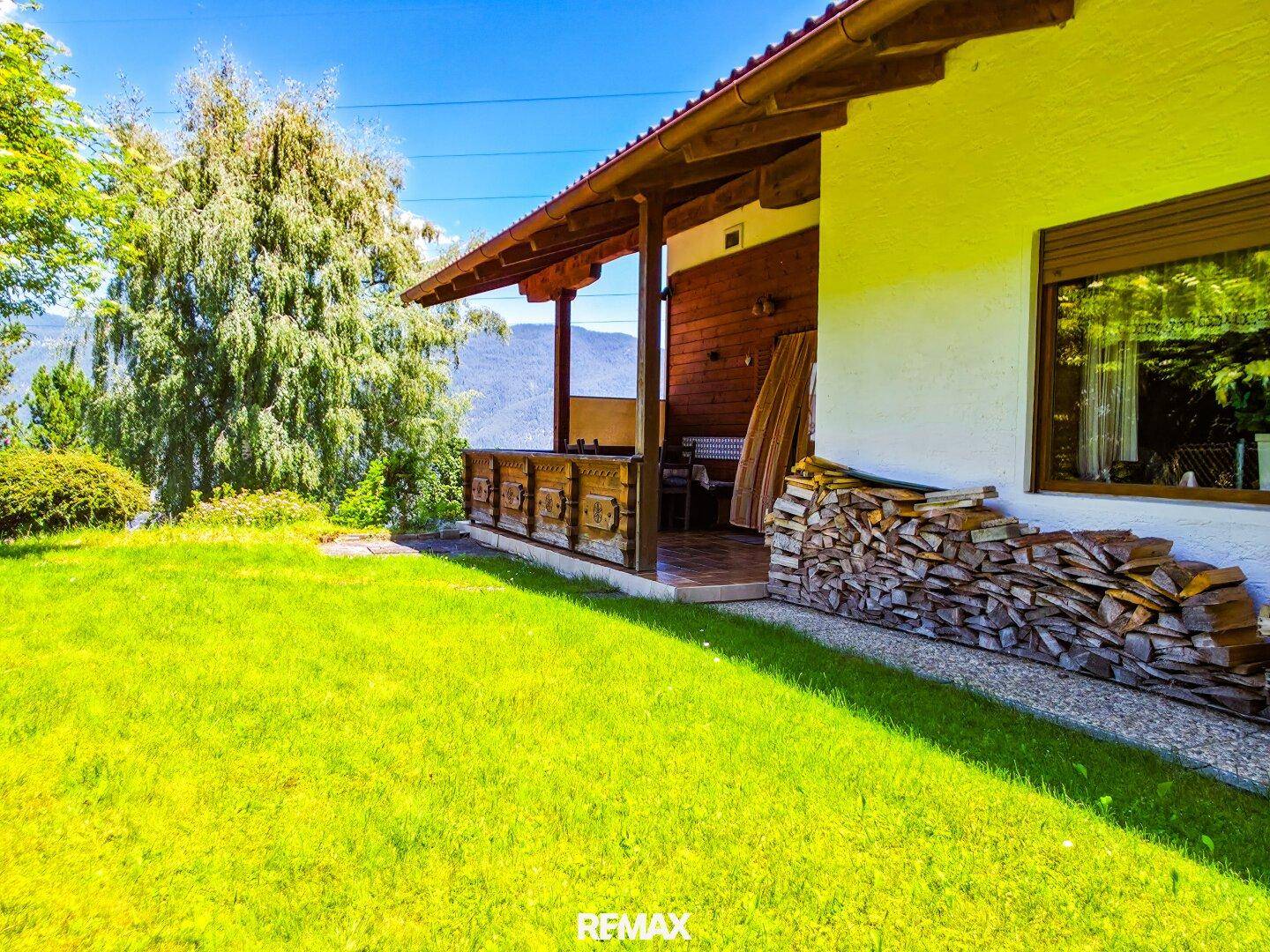 Gemütliche überdachte Loggia am Haus mit Holzstapel und Blick auf die grüne Umgebung.