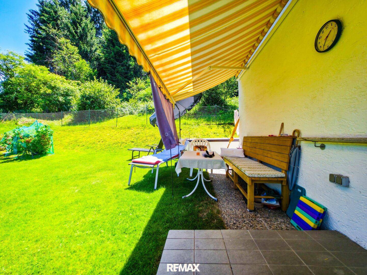 Sonniger Sitzbereich im Garten mit Markise, Gartenmöbeln und weitläufiger Rasenfläche.