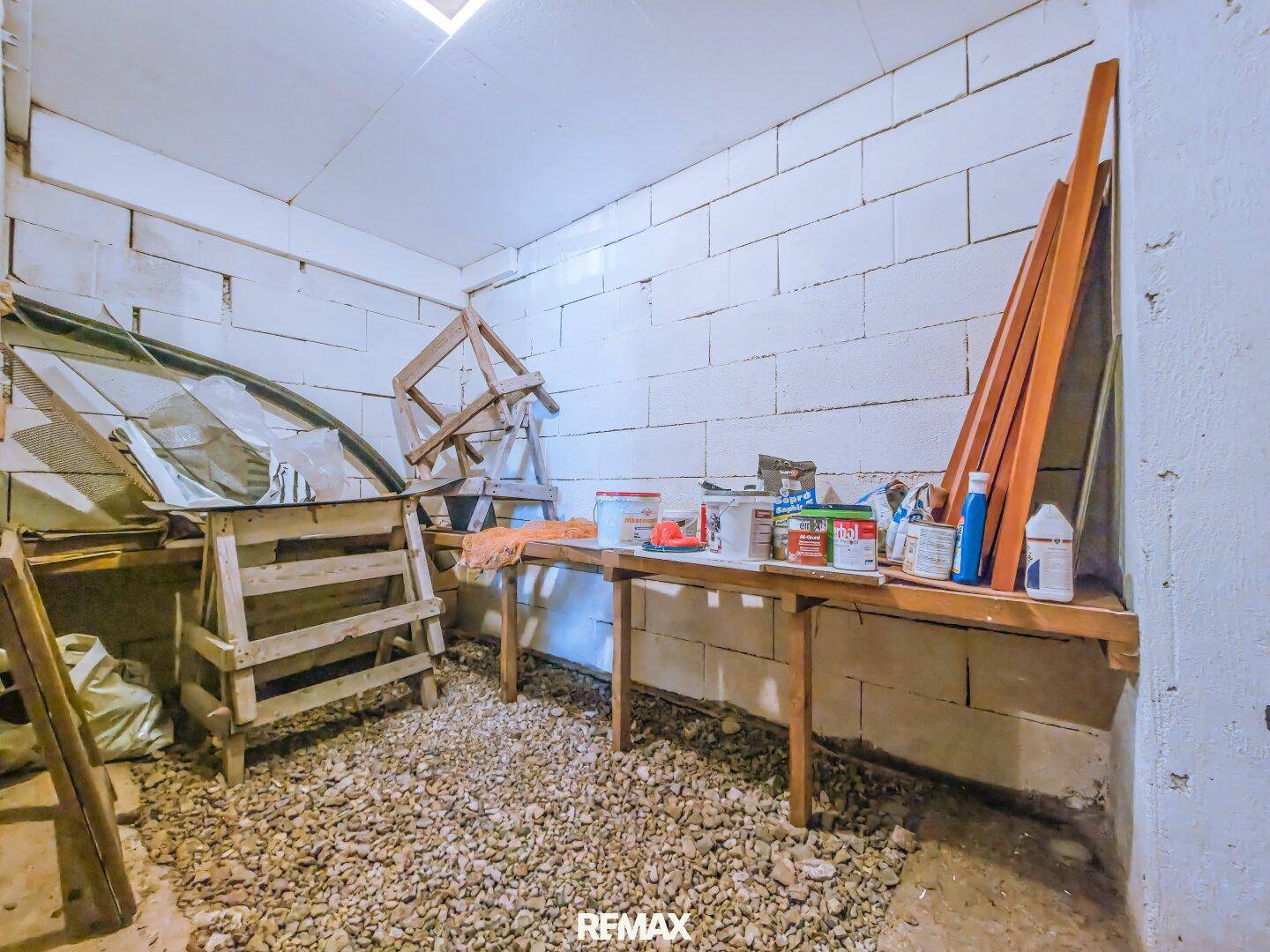 Kellerraum mit Werkbank, Lagerfläche und grobem Kiesboden, ideal für handwerkliche Arbeiten.