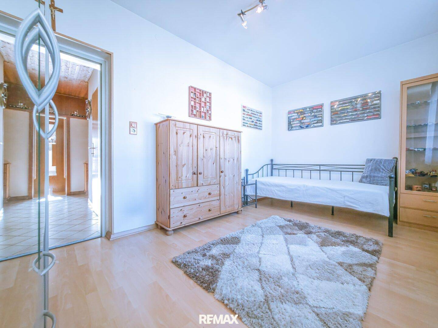 Schlafzimmer mit hellem Parkettboden, Einzelbett und Holzschrank.